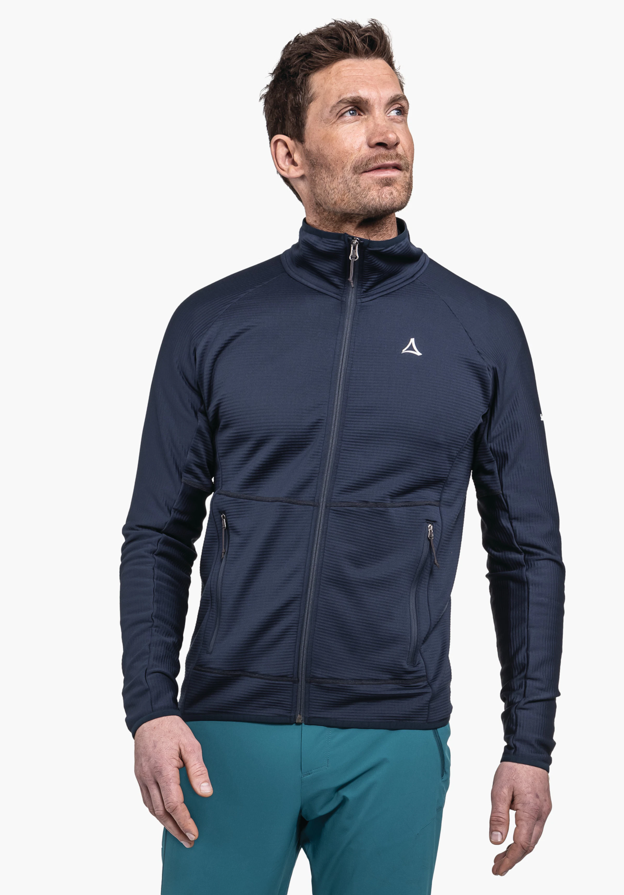 Fleece Jk Style Cascata MNS veste bleu foncé avec logo Schöffel, portée par un homme debout regardant vers le haut à droite; fond blanc; pantalon vert.