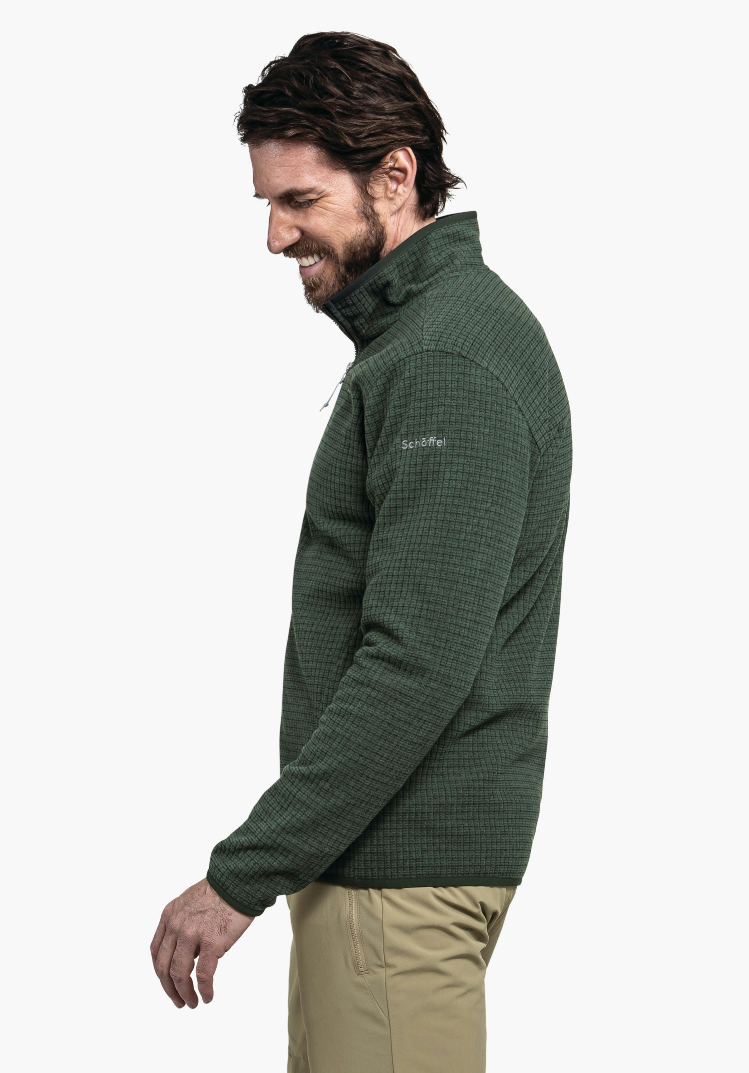 CIRC Fleece Jk Style Terxa MNS dunkelgrüne Jacke; Mann lächelt und schaut nach unten, Arm entspannt, stehend vor weißem Hintergrund. Text auf Ärmel: "Schöffel".