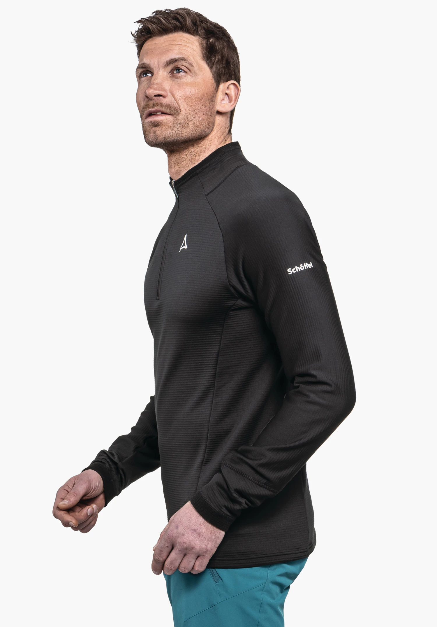Longsleeve Style Cascata MNS man in a black long-sleeve shirt with Schöffel logo on the chest looks upwards; light blue trousers; white background; lettering "Schöffel" on sleeve.