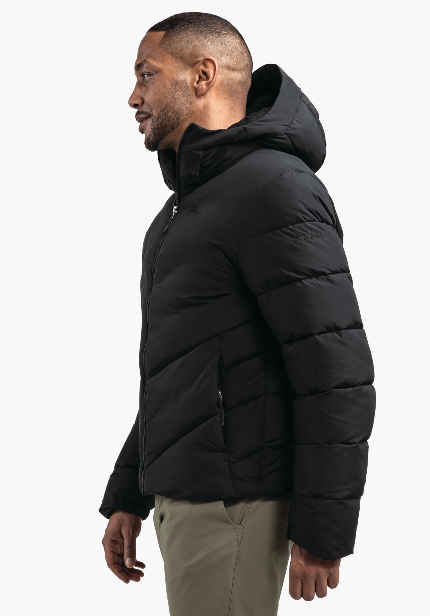 Ins Jacket Style Lodos MNS veste matelassée noire à capuche portée par un homme debout en profil latéral devant fond blanc; logo Schöffel sur la poitrine; inscription "Schöffel" sur la manche.