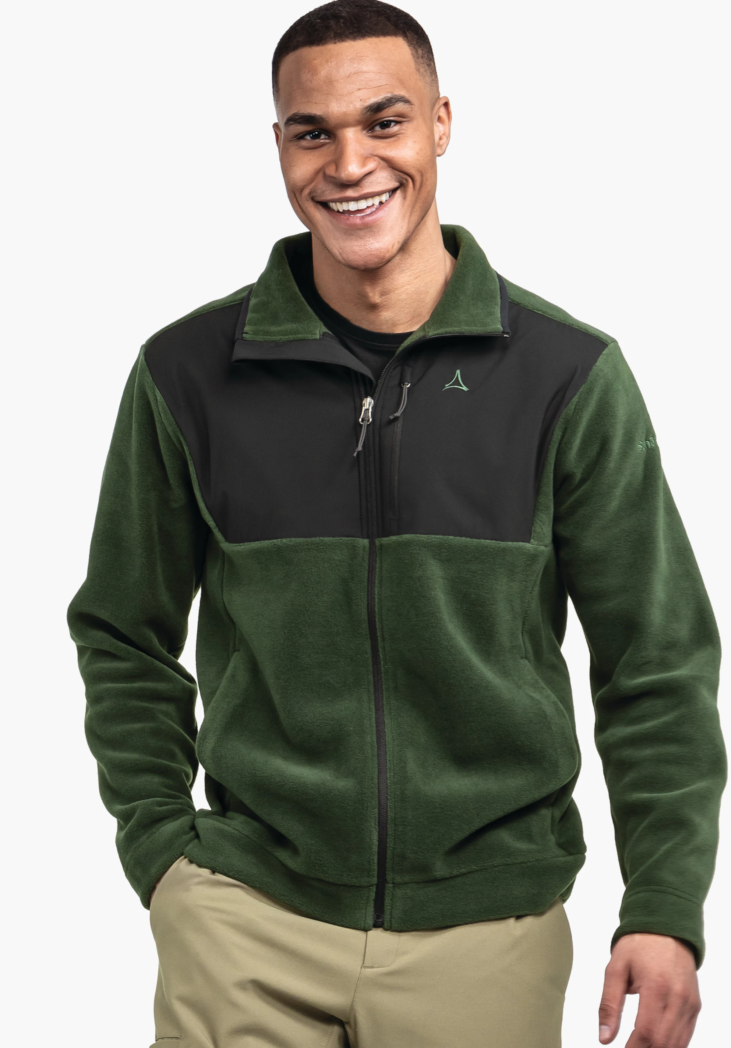 Fleece Jk Style Gregale MNS Veste polaire vert foncé avec empiècement poitrine noir et logo Schöffel, portée par une personne souriante debout de manière détendue, mains dans le pantalon marron clair, fond blanc.
