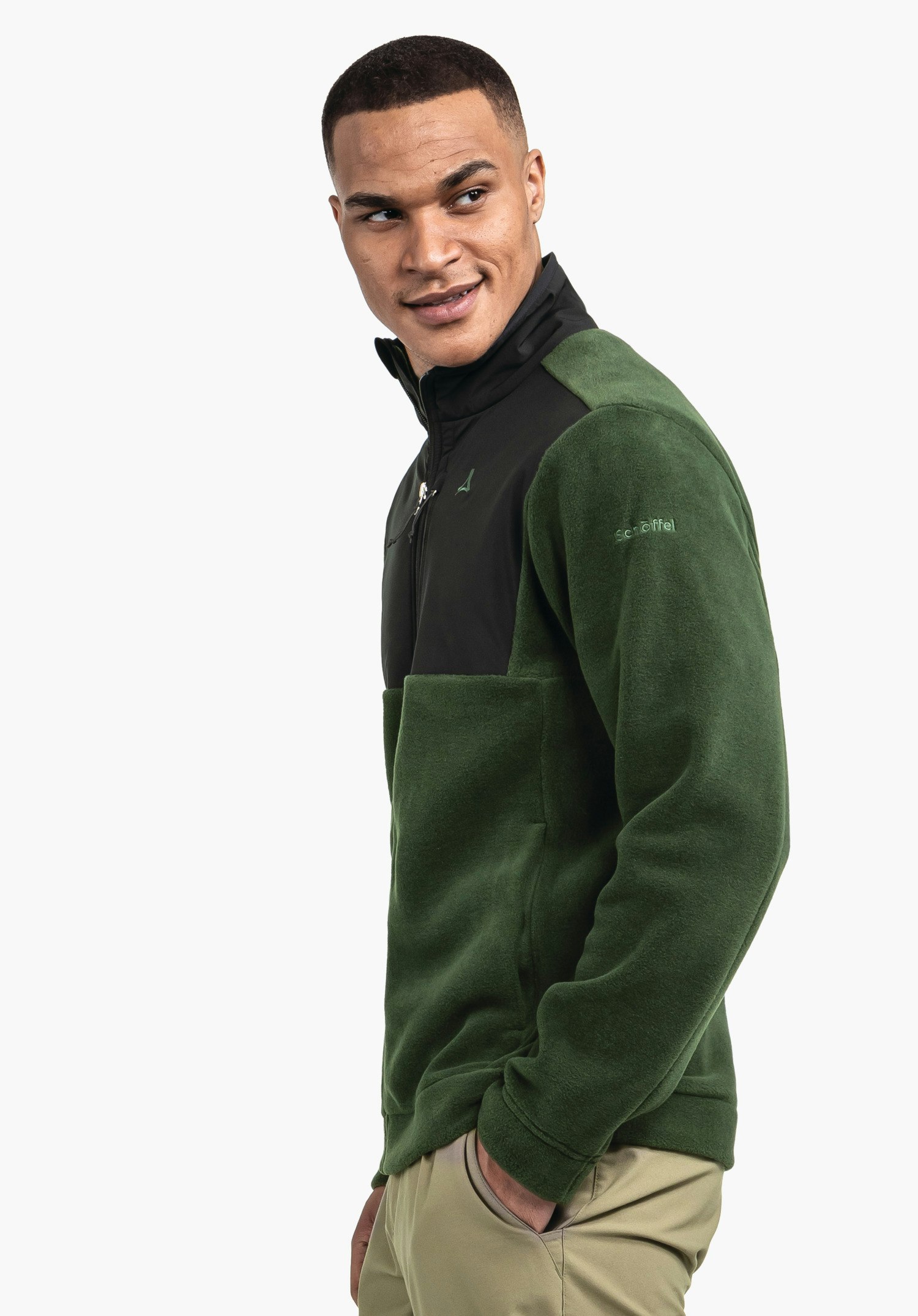 Fleece Jk Style Gregale MNS dunkelgrüne Fleecejacke mit schwarzem Brustteil, getragen von Mann, dreht sich lächelnd zur Seite; Schöffel-Logo auf Brust, Schriftzug "schöffel" auf Ärmel; weißer Hintergrund.