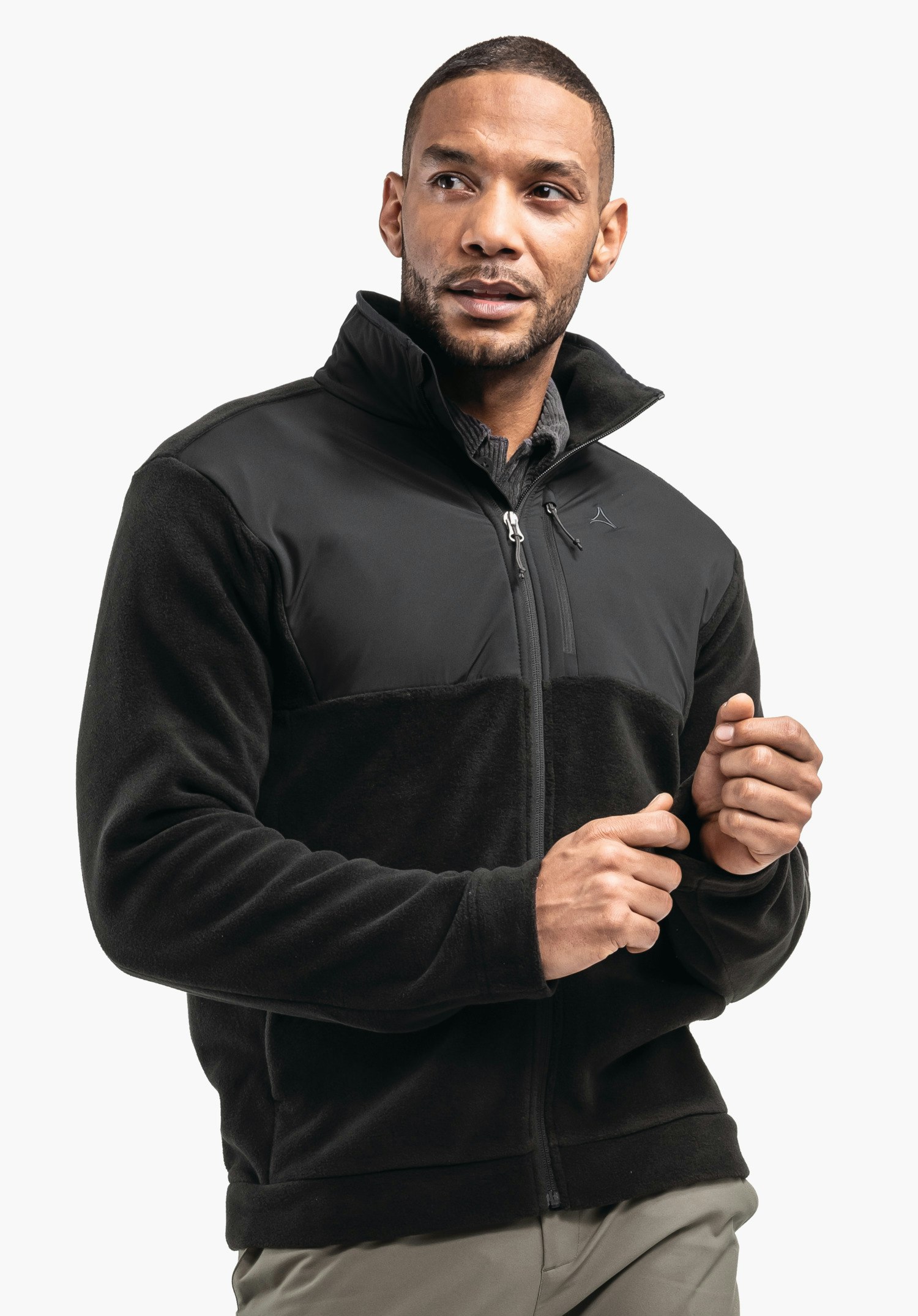 Fleece Jk Style Gregale MNS Mann trägt schwarze Fleecejacke mit Schöffel-Logo, zieht am Reißverschluss; steht vor schlichtem weißem Hintergrund, trägt hellgraue Hose.