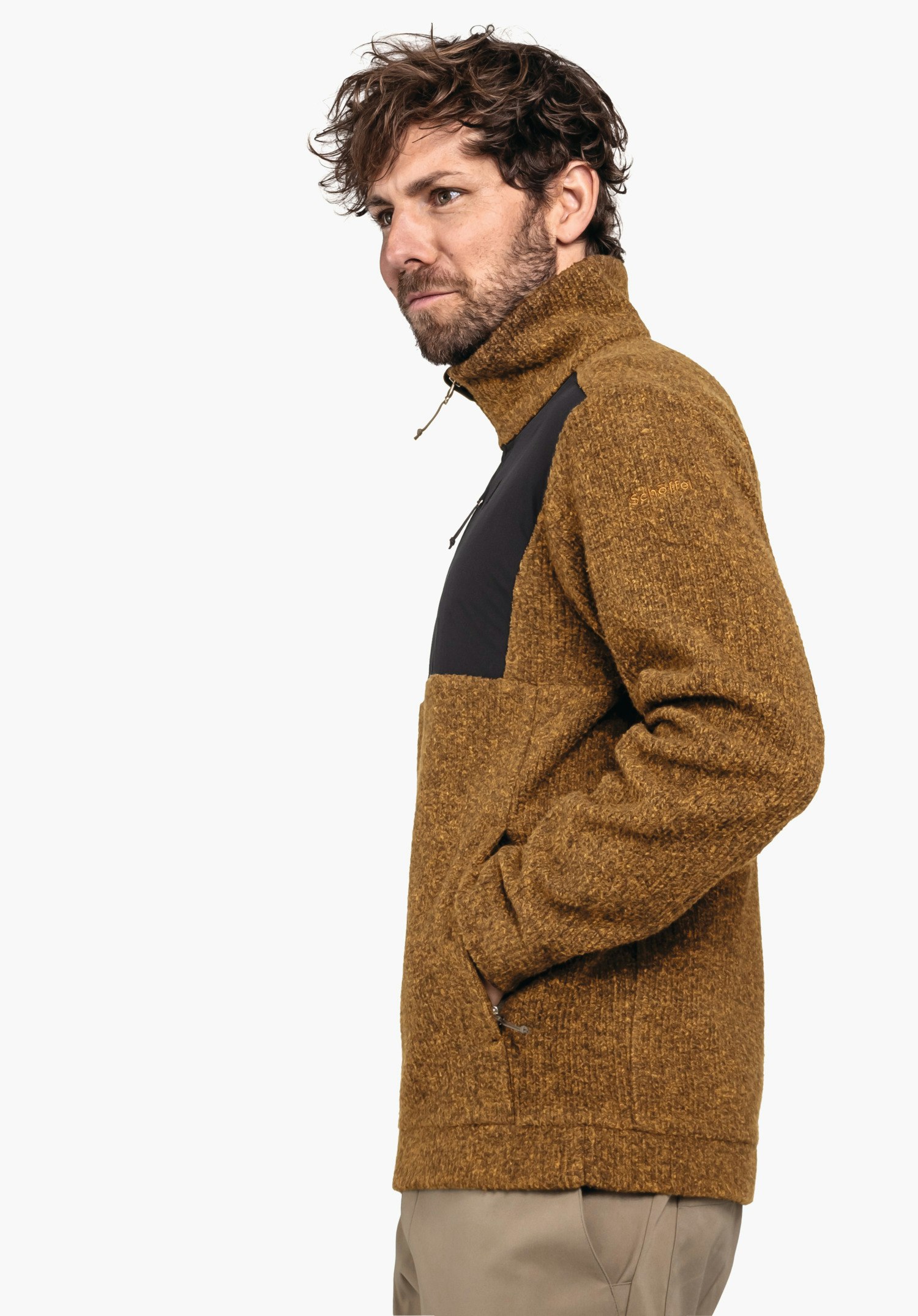 Fleece Jk Style Canterbury MNS Jacke: Mann trägt dunkelgelbe Strickjacke mit schwarzem Brustpanel, steht seitlich mit Händen in Taschen vor hellgrauem Hintergrund. Text: "Schöffel".