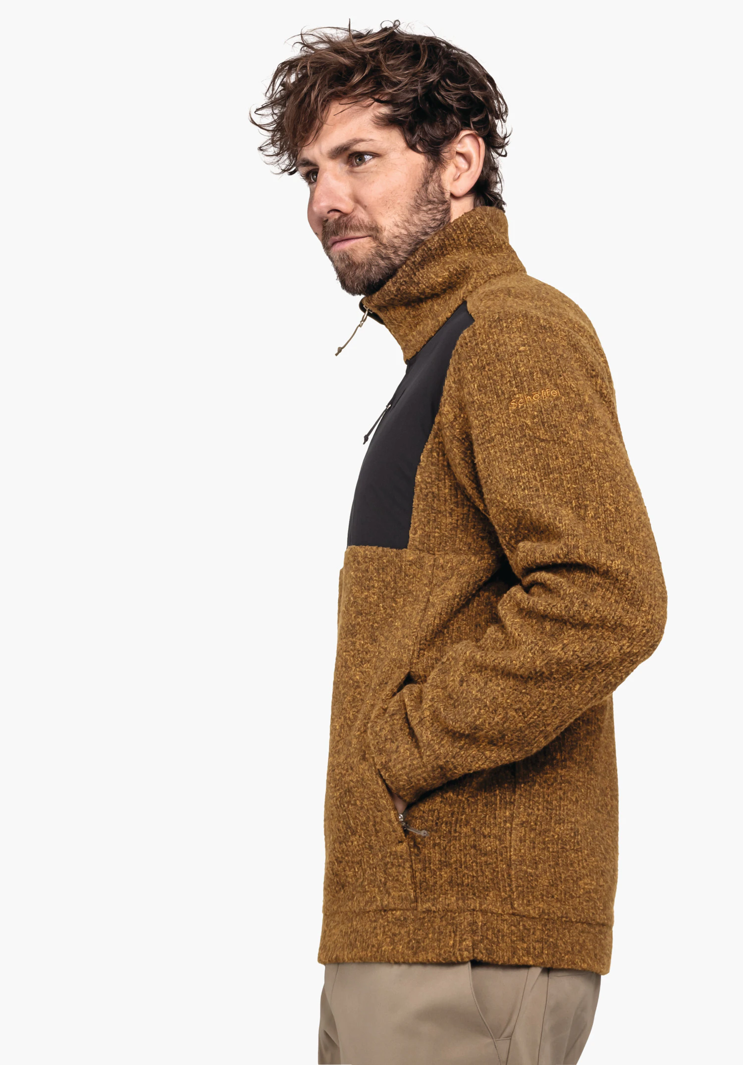 Fleece Jk Style Canterbury MNS jacket worn by a man wearing a dark yellow knitted jacket with black chest panel, stands side-on with hands in pockets in front of a light grey background. Text: "Schöffel"., Fleece Jk Style Canterbury MNS jacket worn by a man wearing a dark yellow knitted jacket with black chest panel, stands side-on with hands in pockets in front of a light grey background. Text: "Schöffel".