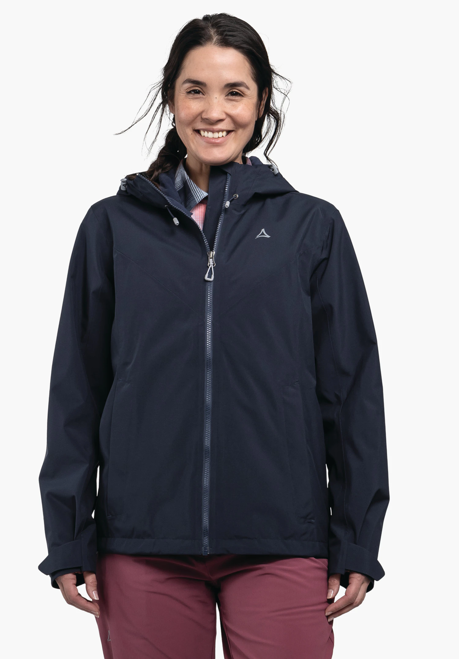 Jacket Style Yew WMS Dunkelblaue Jacke mit Schöffel-Logo, von einer lächelnden Frau getragen; Reißverschluss geschlossen, Kapuze anliegend, steht vor weißem Hintergrund, kombiniert mit rosa Hose.