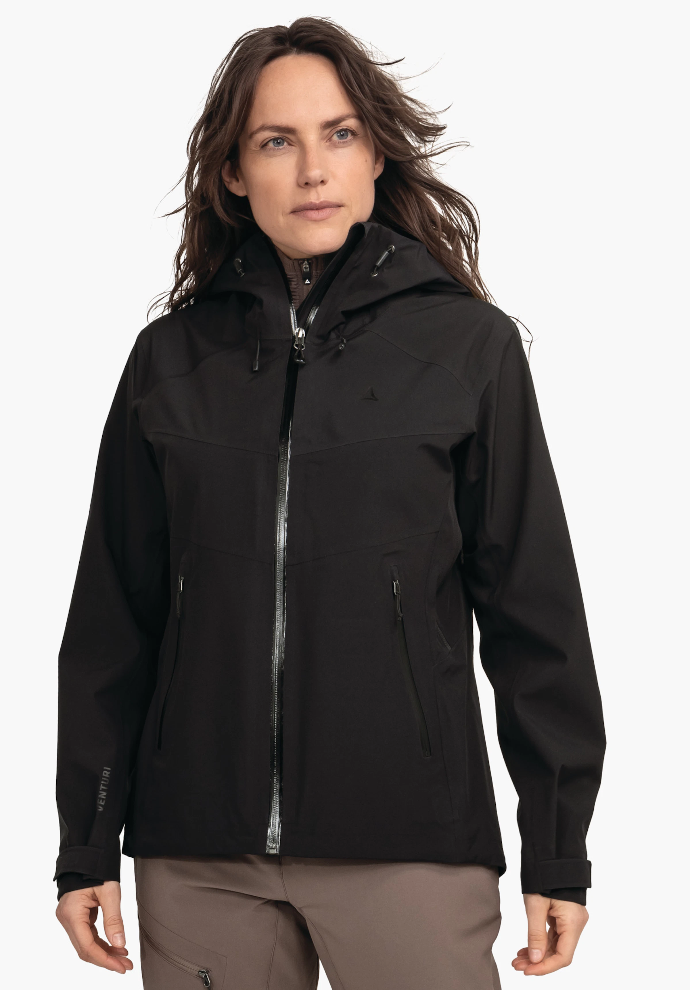 Jacket Style Cascata WMS Veste de pluie noire à capuche avec logo Schöffel sur la poitrine, portée par une femme; zip fermé, poches zippées; pantalon marron clair, fond blanc. Texte: VENTURI.