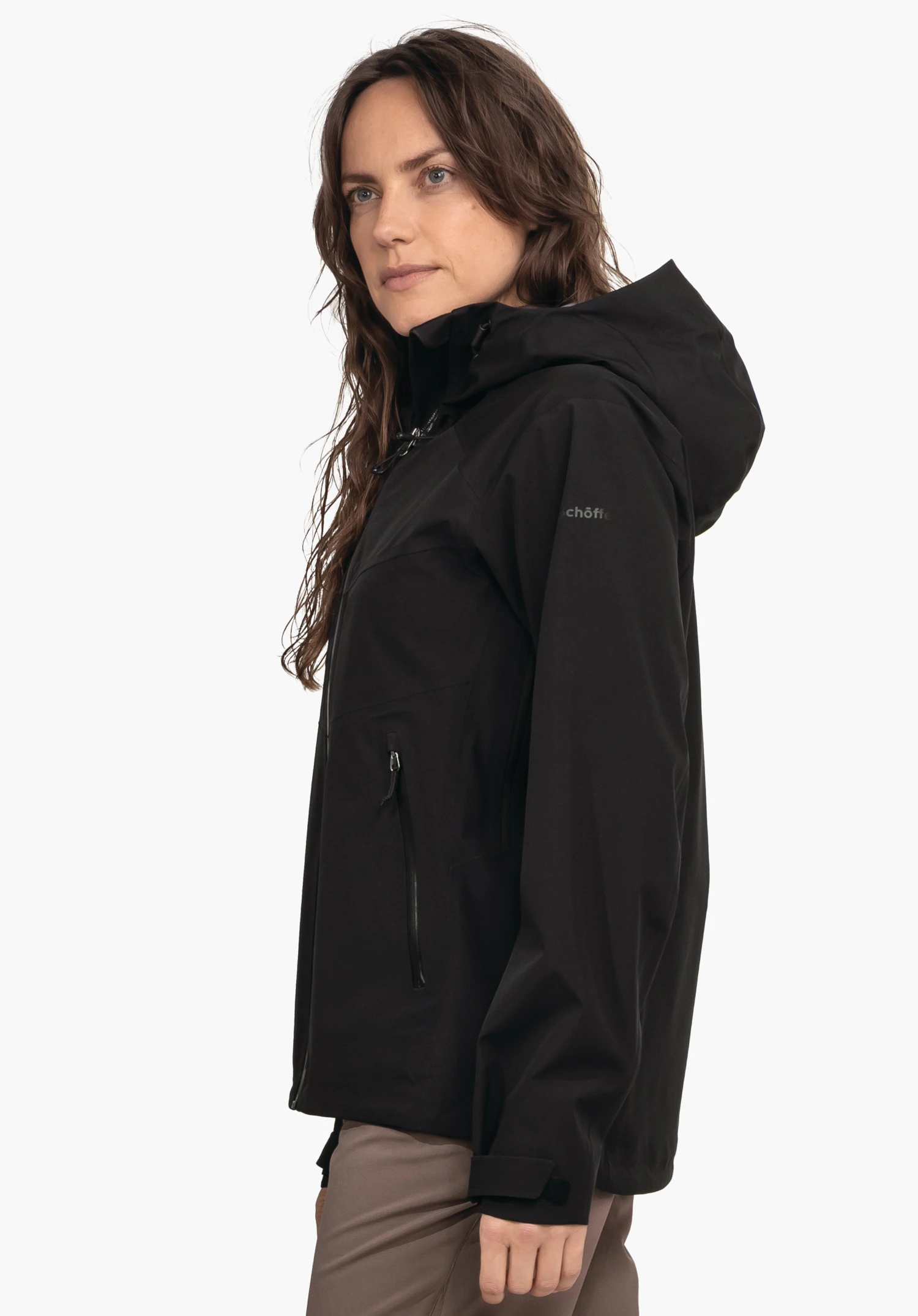 Jacket Style Cascata WMS femme portant une veste noire à capuche, debout de profil et regardant vers l’avant devant fond clair. Texte sur la manche: "schöffel".