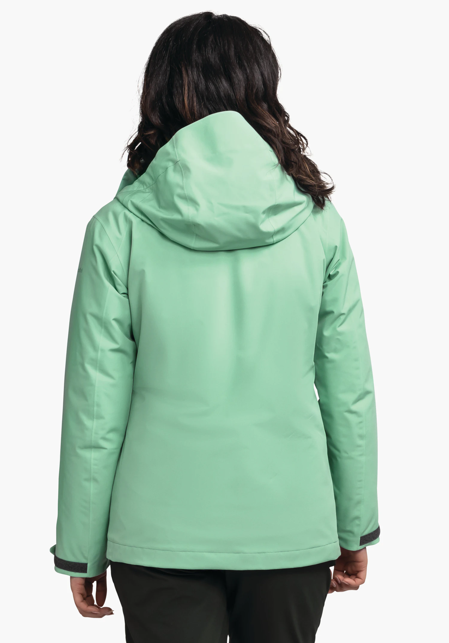 3in1 Jacket Style Tamina WMS lichtgroene jas, gedragen door een persoon die met de rug naar de camera staat, capuchon op, handen langs het lichaam, donker haar zichtbaar, neutrale lichte achtergrond.