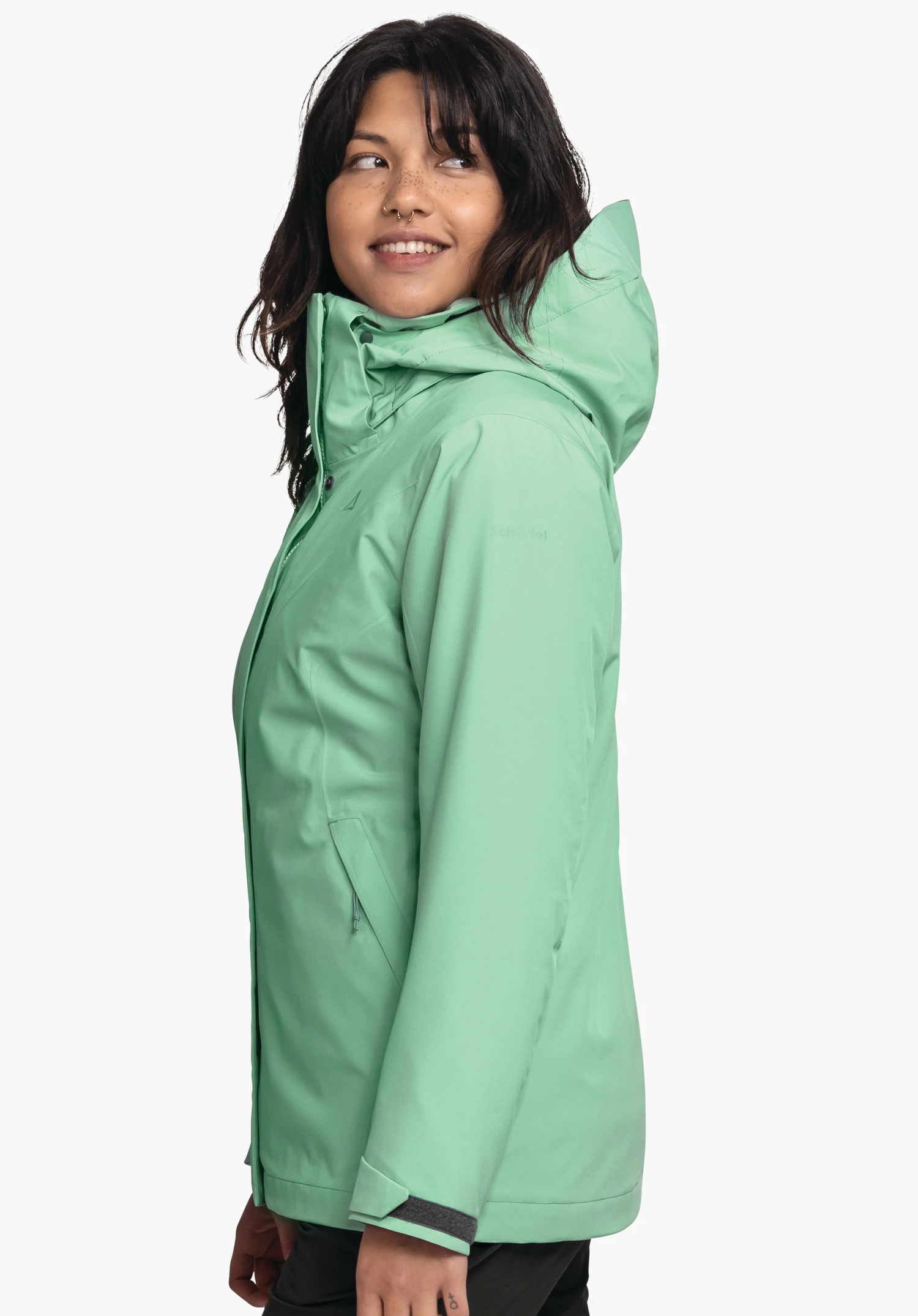 3in1 Jacket Style Tamina WMS lichtgroene outdoorjas met capuchon, gedragen door een vrouw die zijwaarts glimlachend kijkt; Schöffel-logo op de borst, tekst "Schöffel" op de mouw; witte achtergrond.