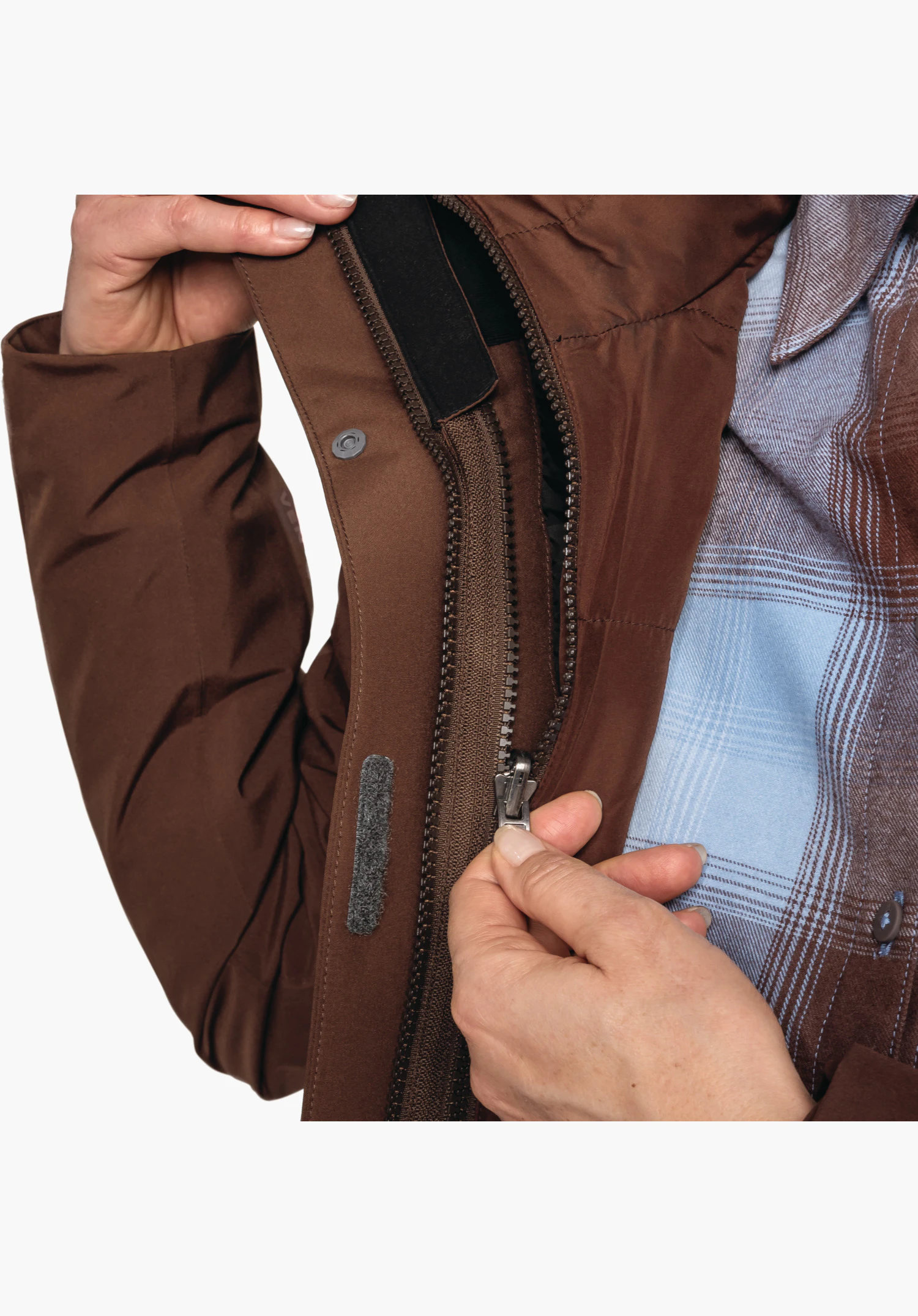 3in1 Jacket Style Tamina WMS zeigt Hände beim Verstellen des Kordelzugs am Saum der braunen Jacke, Nahaufnahme vor weißem Hintergrund.
