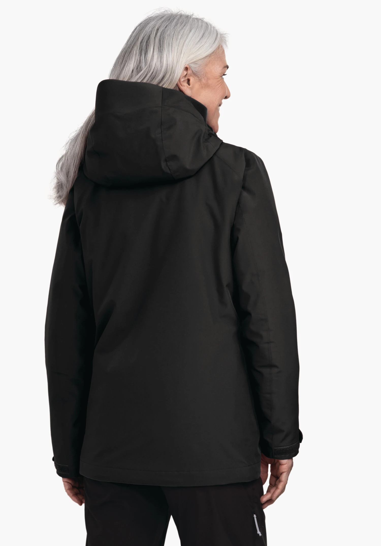 3in1 Jacket Style Tamina WMS zwarte jas met capuchon, van achteren gedragen; vrouw met lichtgrijs haar kijkt naar rechts en glimlacht; neutrale witte achtergrond., 3in1 Jacket Style Tamina WMS zwarte jas met capuchon, van achteren gedragen; vrouw met lichtgrijs haar kijkt naar rechts en glimlacht; neutrale witte achtergrond.