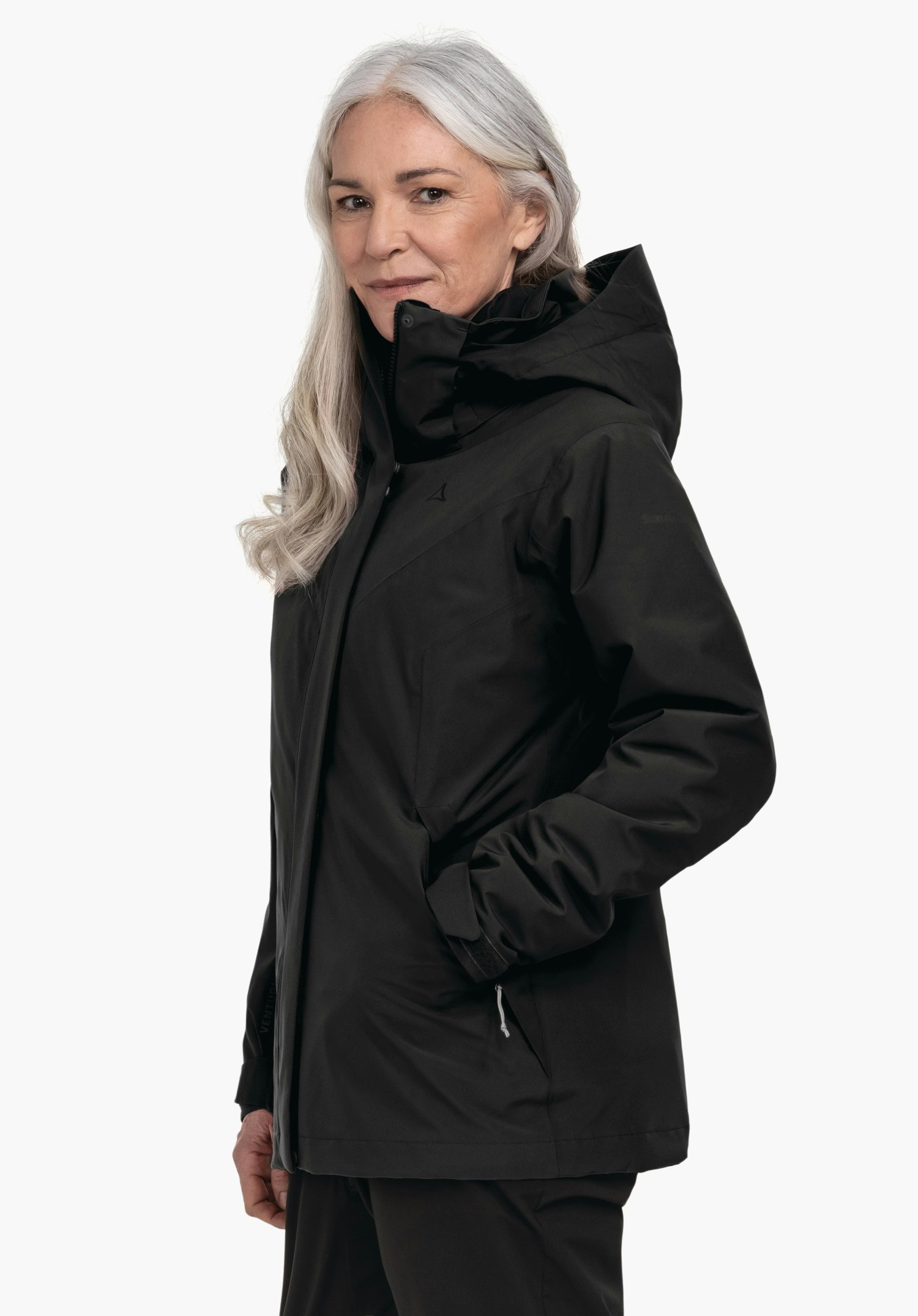 3in1 Jacket Style Tamina WMS veste noire portée par une femme aux cheveux blanc clair; logo Schöffel sur la poitrine, mains dans les poches, devant fond clair.