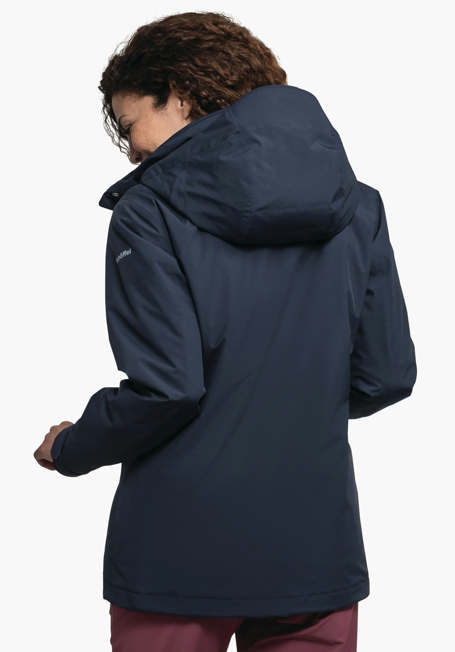 3in1 Jacket Style Tamina WMS veste bleu foncé, portée par une personne se retournant et regardant vers la gauche; capuche reposant sur le dos; fond blanc. Texte sur la manche: « Schöffel ».