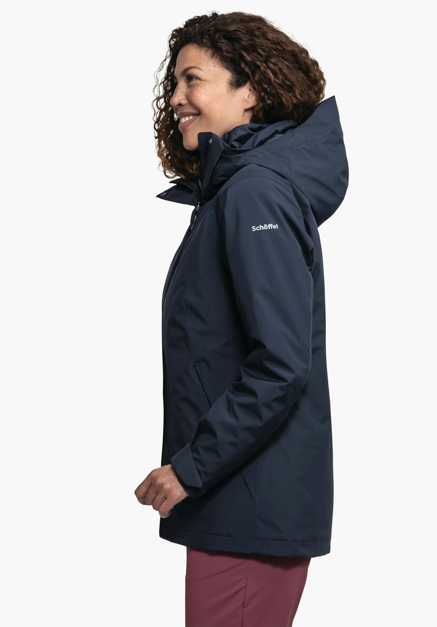 3in1 Jacket Style Tamina WMS veste bleu foncé portée par une femme souriante en profil, debout devant fond blanc; impression sur la manche: "Schöffel". Pantalon rouge visible.