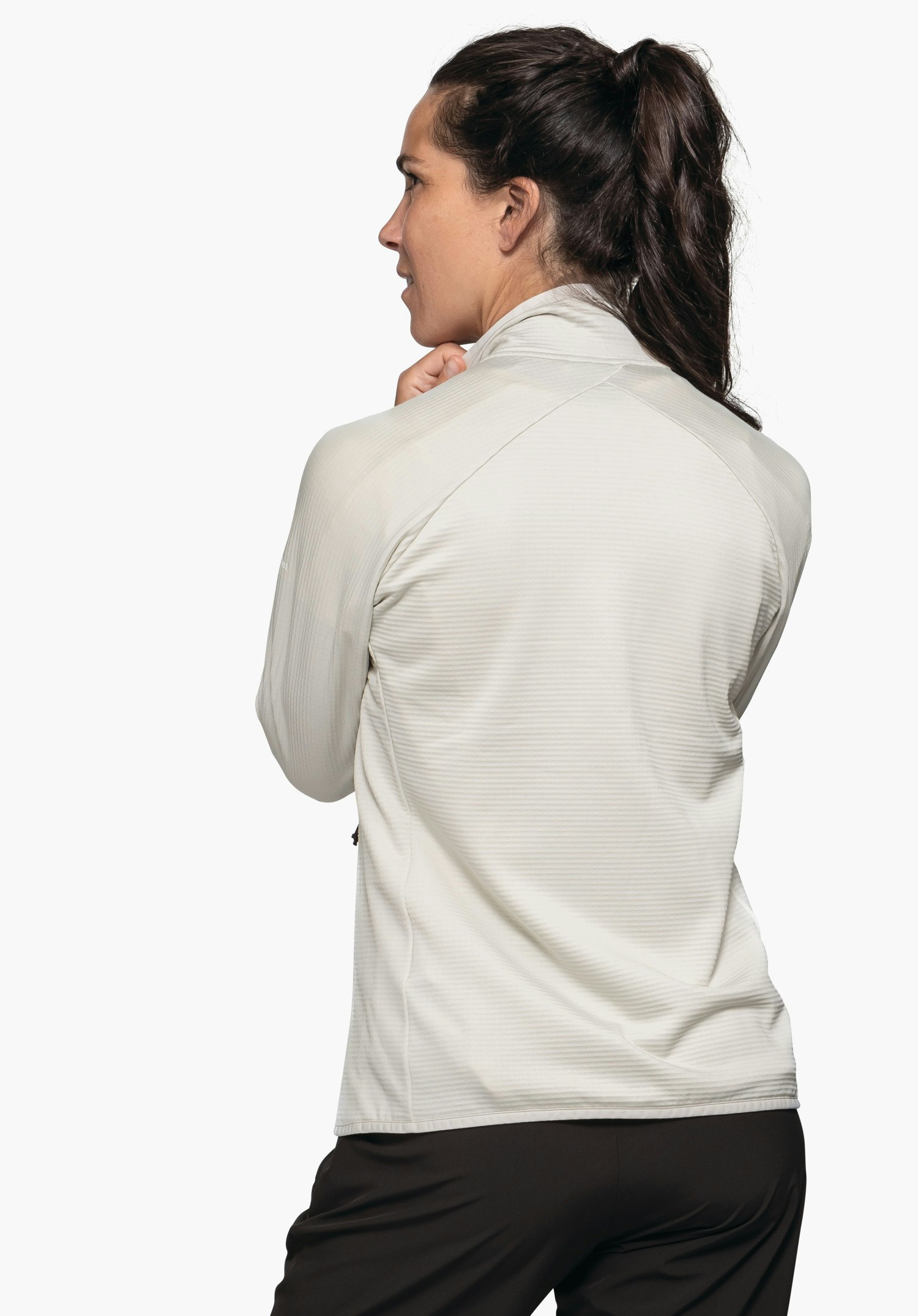 Fleece Jk Style Cascata WMS femme portant une veste blanche se tournant légèrement sur le côté et tenant le col; fond clair neutre, pantalon noir.