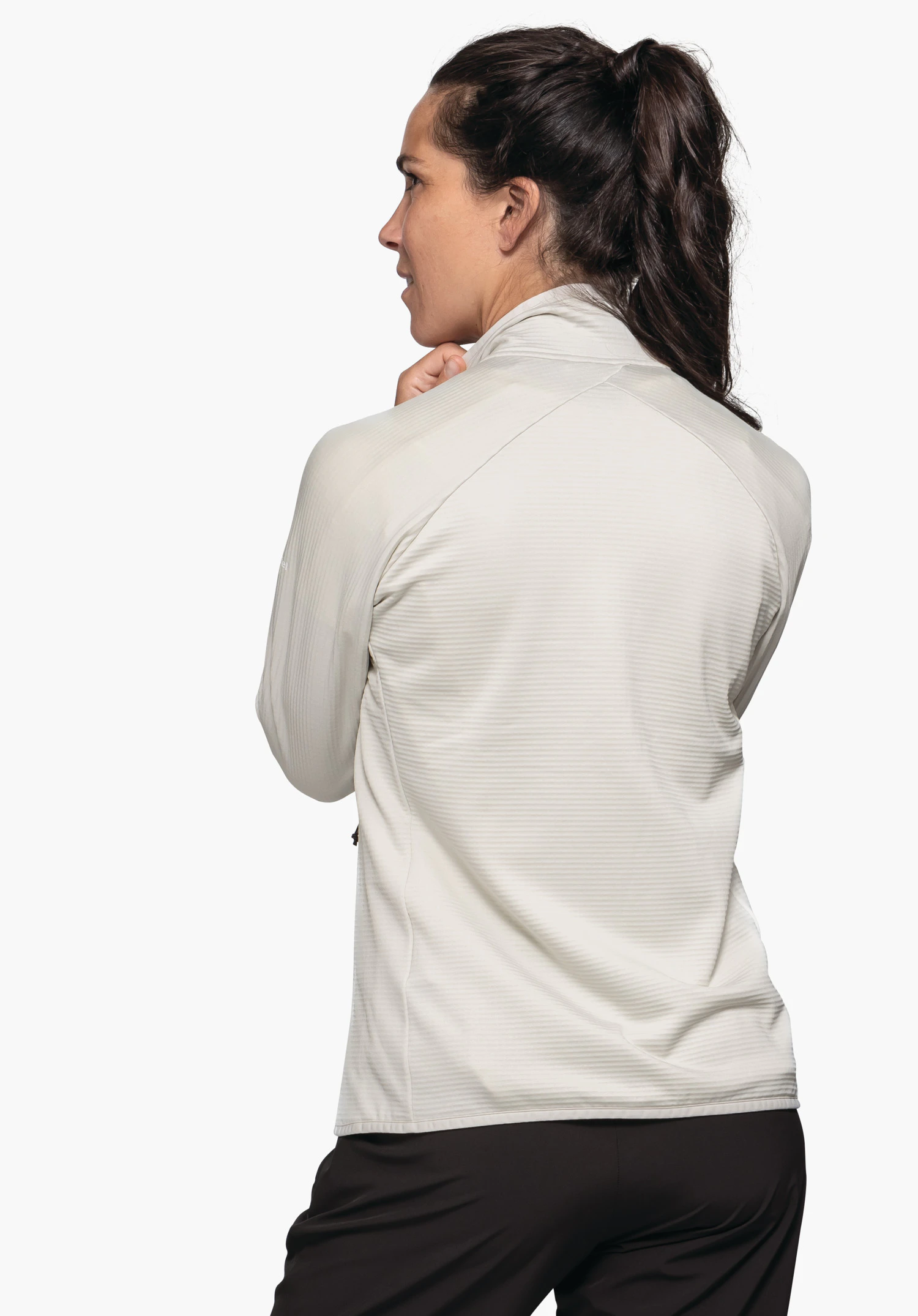 Fleece Jk Style Cascata WMS woman in a white jacket turns sideways and holds the collar; light neutral background, wearing black trousers.