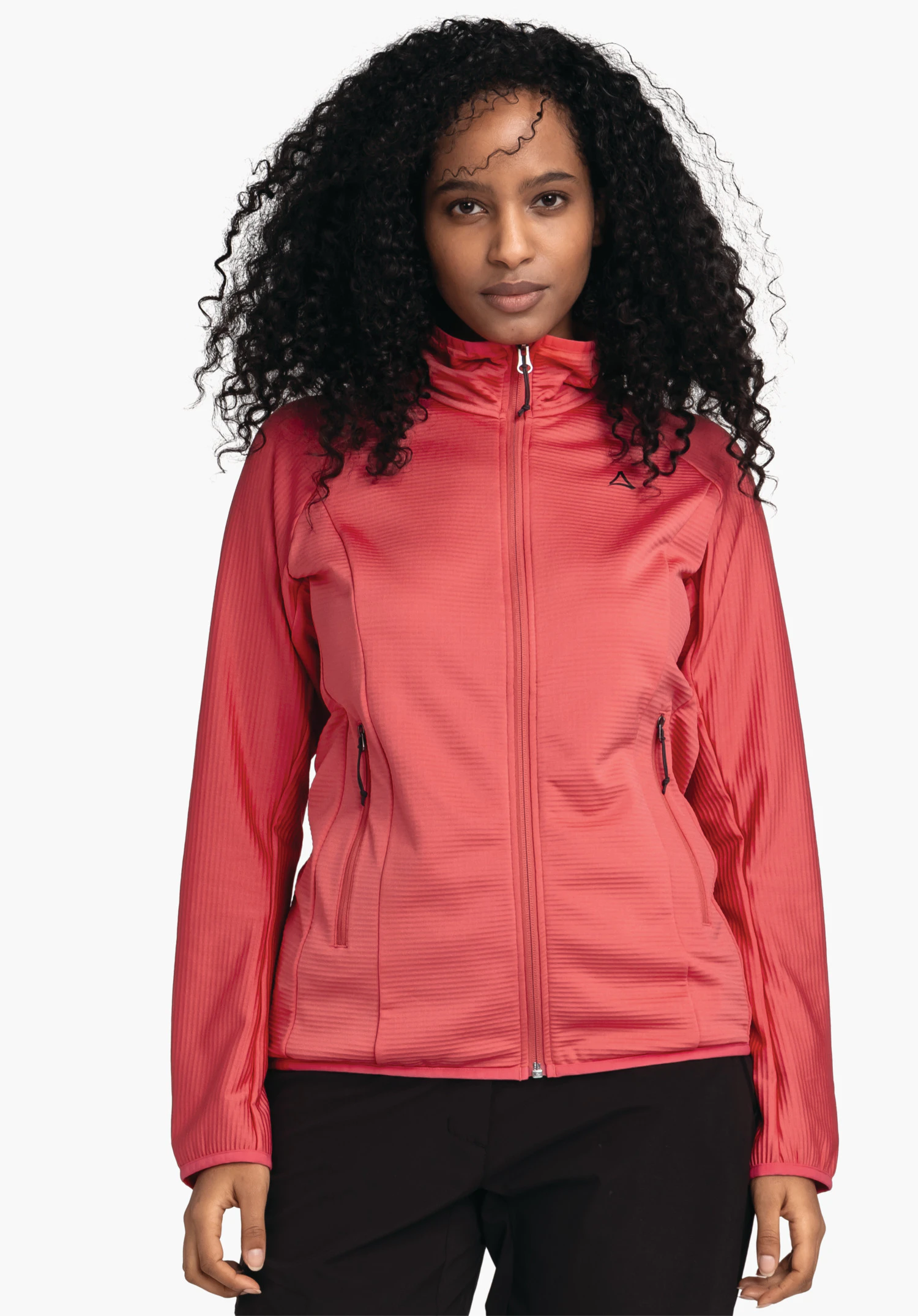 Fleece Jk Style Cascata WMS Veste rouge clair portée de face par une femme; zip fermé, logo Schöffel sur la poitrine gauche; femme aux cheveux noirs bouclés, pantalon noir, fond blanc.