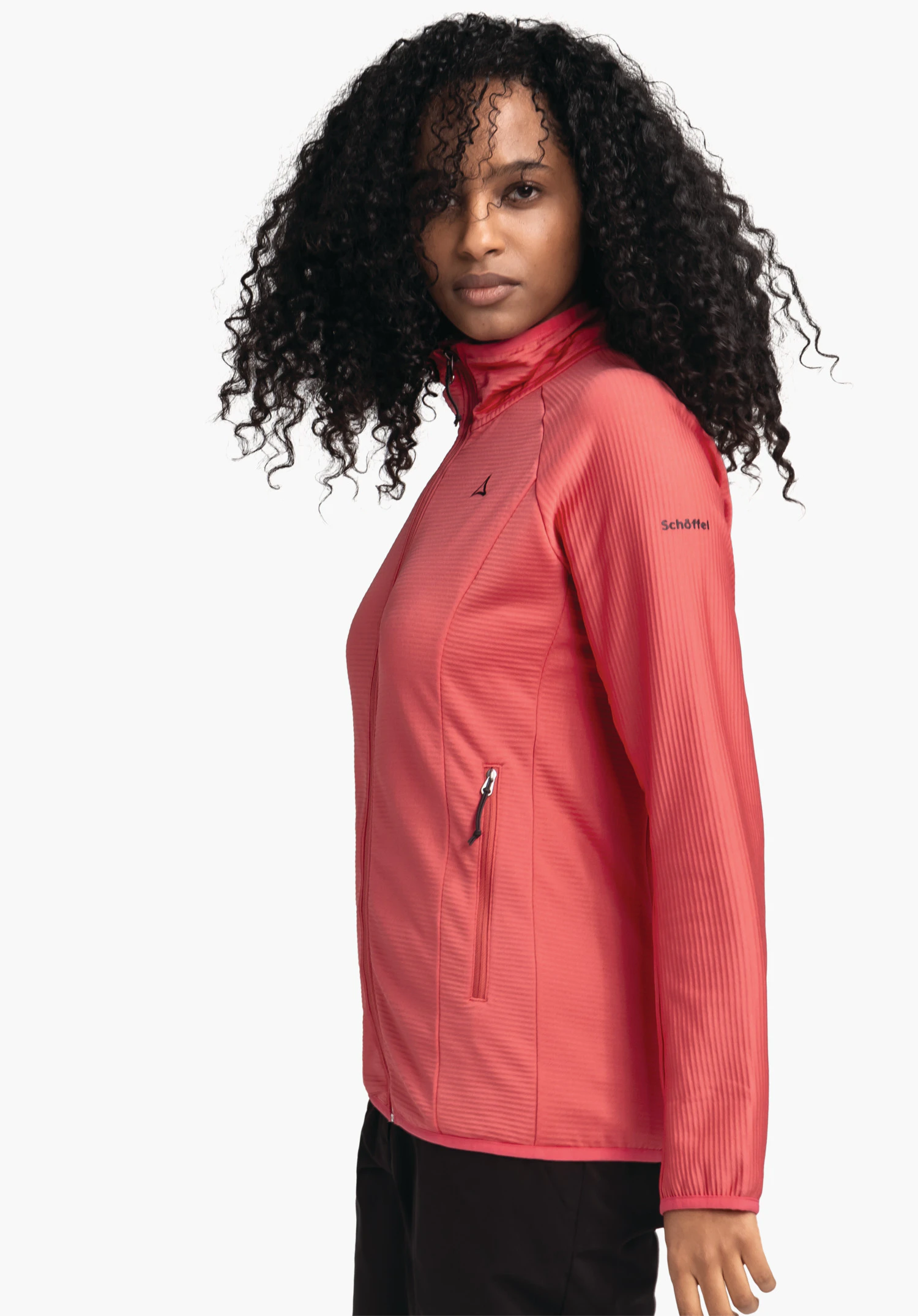 Fleece Jk Style Cascata WMS veste softshell rouge clair portée par une femme debout de profil, regard vers la caméra; logo Schöffel sur la poitrine, inscription "Schöffel" sur la manche; fond blanc.