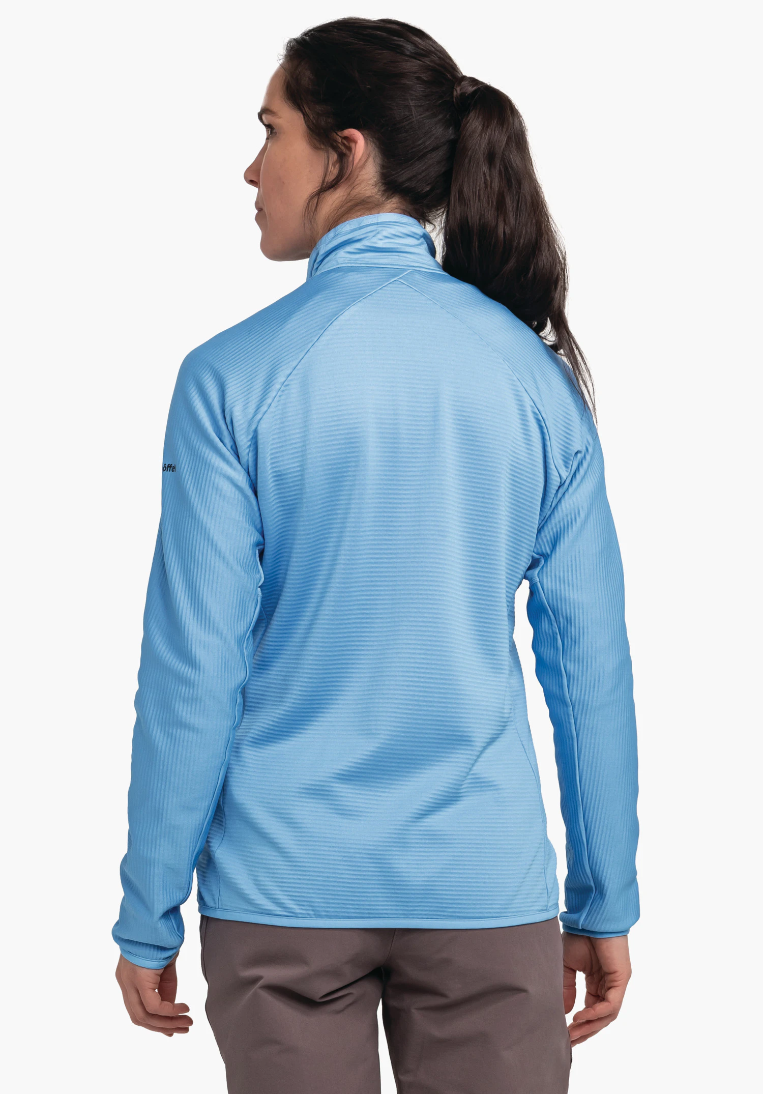 Fleece Jk Style Cascata WMS light blue jacket; woman stands with her back to the camera, head turned left; neutral white studio background. Sleeve text: “Schöffel”.
