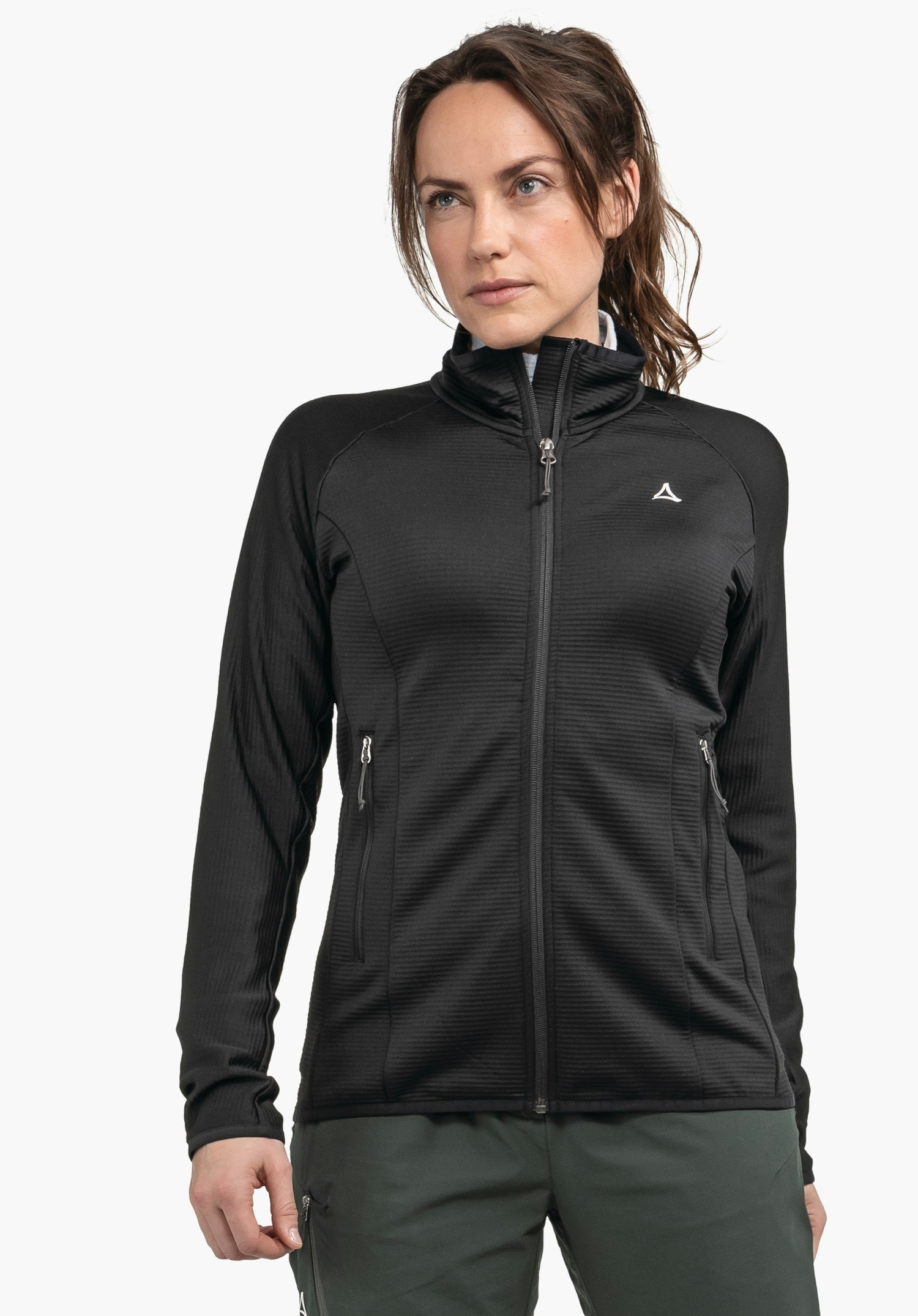 Fleece Jk Style Cascata WMS Femme portant une veste noire avec logo Schöffel, debout de face et regardant vers la droite; bras détendus, pantalon vert foncé; fond clair neutre.