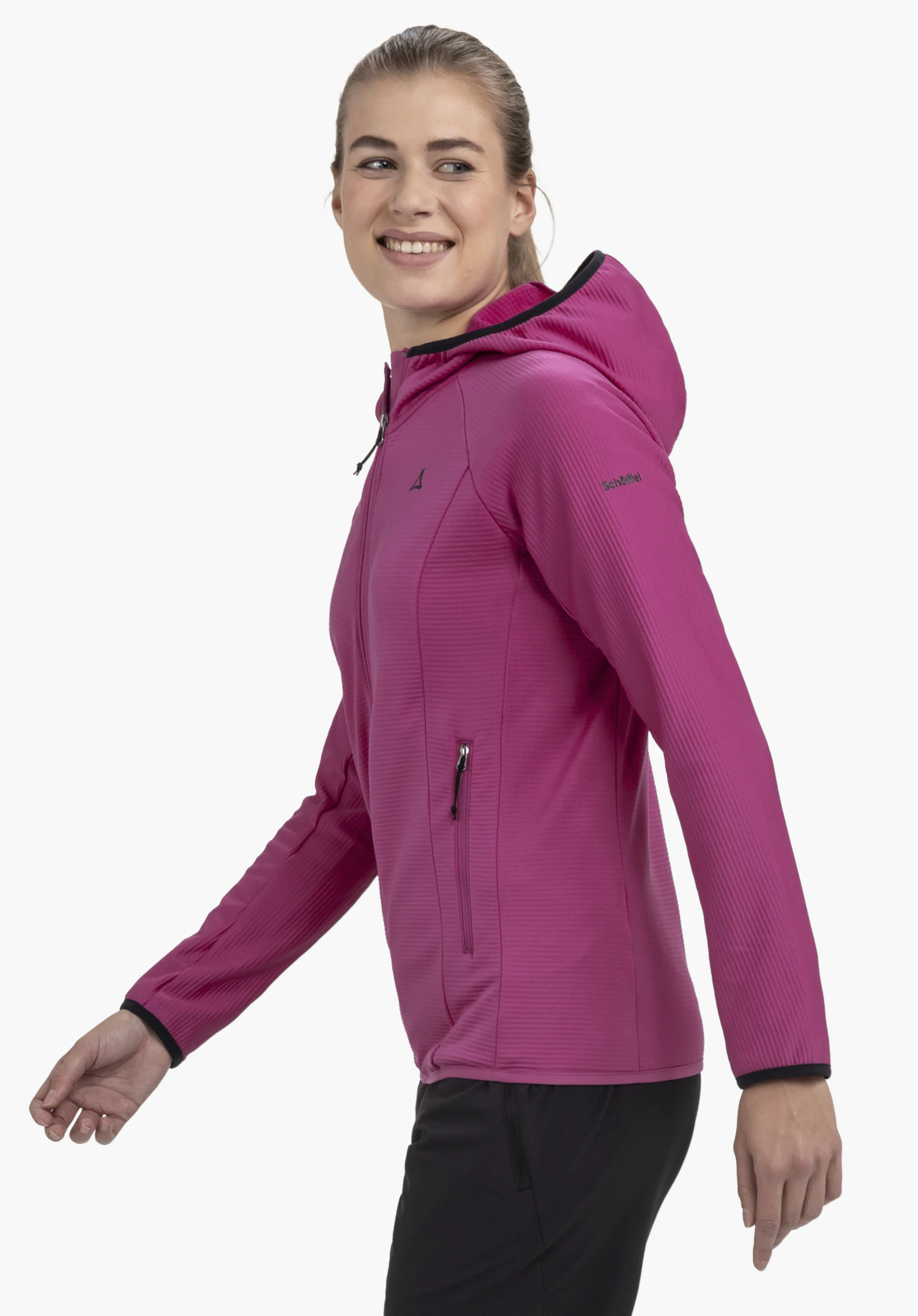 Fleece Hoody Style Cascata WMS is worn by a model standing sideways and smiling at the camera. The pink jacket shows the Schöffel-Logo on the chest and the left sleeve, presented against a neutral background.