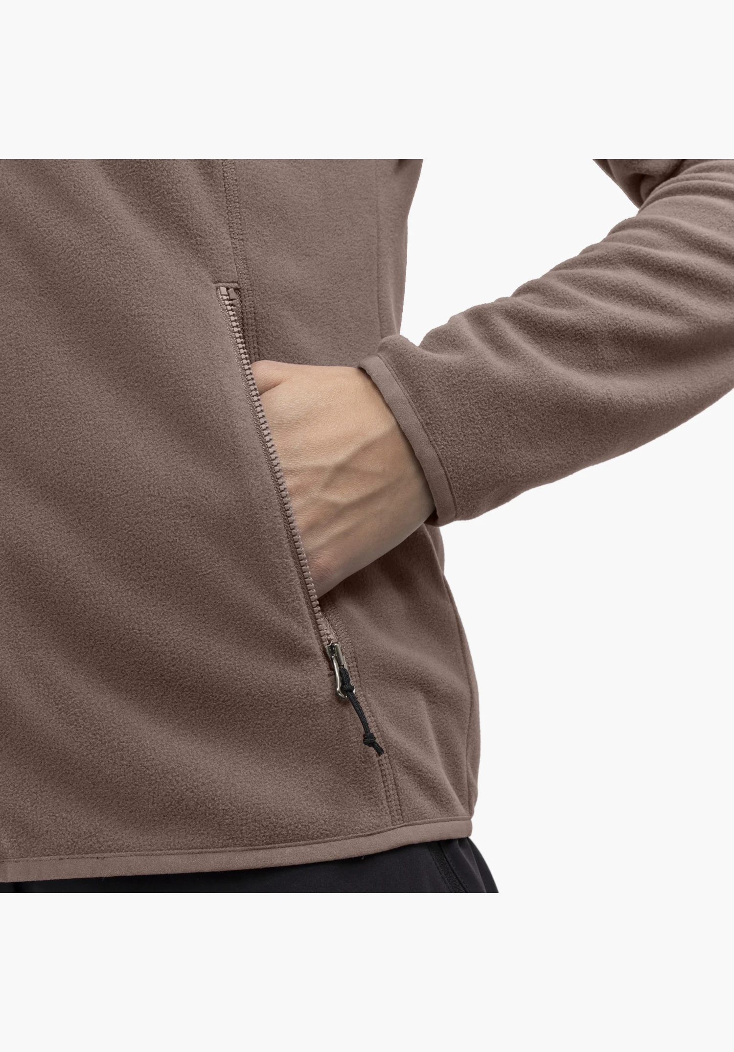 Fleece Jk Style Ash WMS, detail view of the side pocket zip with a hand resting inside the soft, brown fleece fabric. Close-up against a white/neutral background.