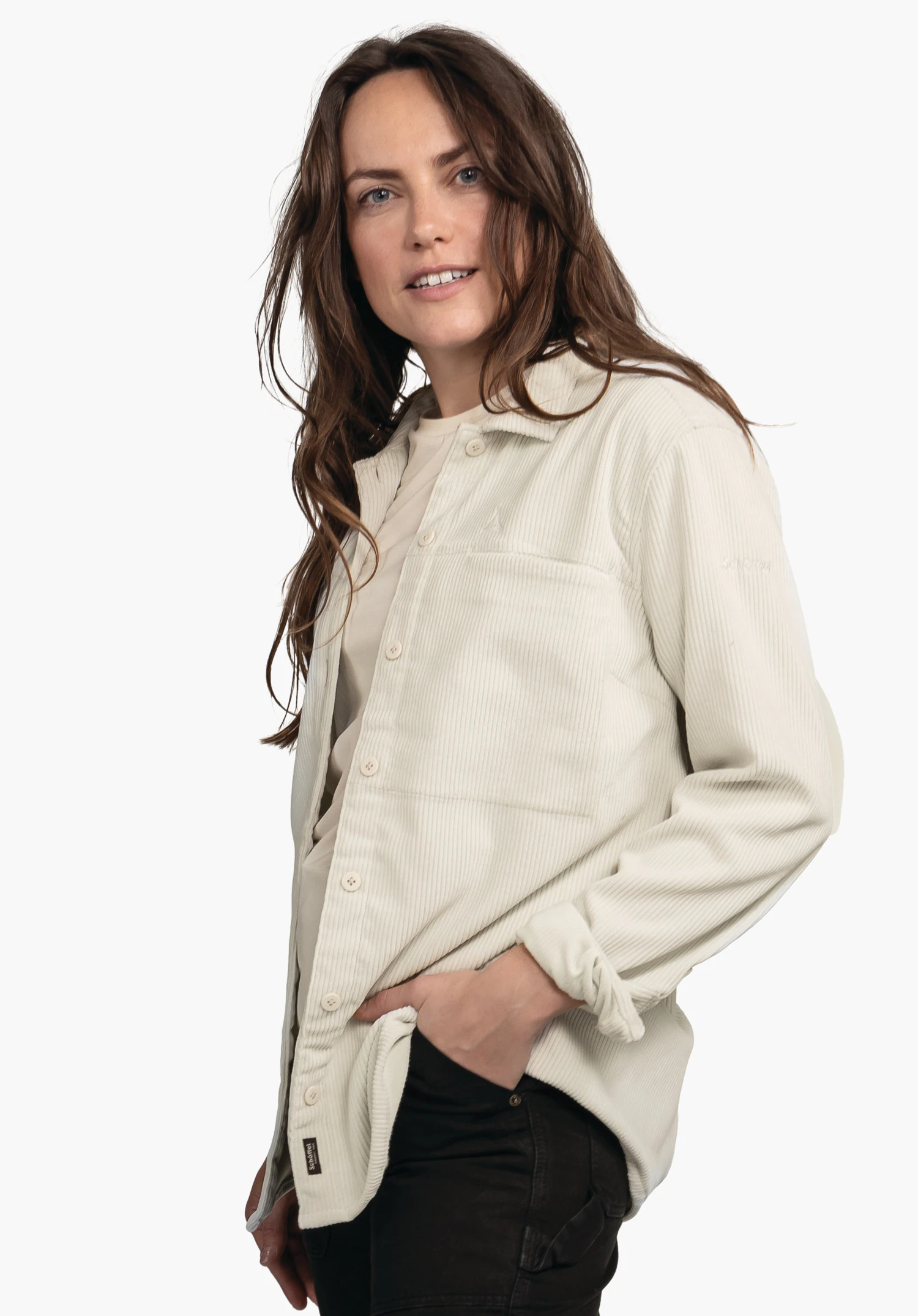 Blouse Style Lodos WMS lichtwitte corduroy overhemdjas; vrouw draagt deze glimlachend met een hand in de zak van een zwarte broek, voor een egaal witte achtergrond.