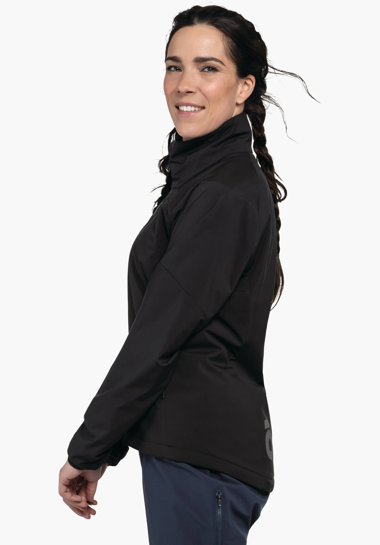Ins Jacket Style Salza WMS zwarte jas, gedragen door een zijwaarts staande vrouw die licht glimlacht; context: witte studioachtergrond, omgeslagen kraag, donkerblauwe broek zichtbaar.