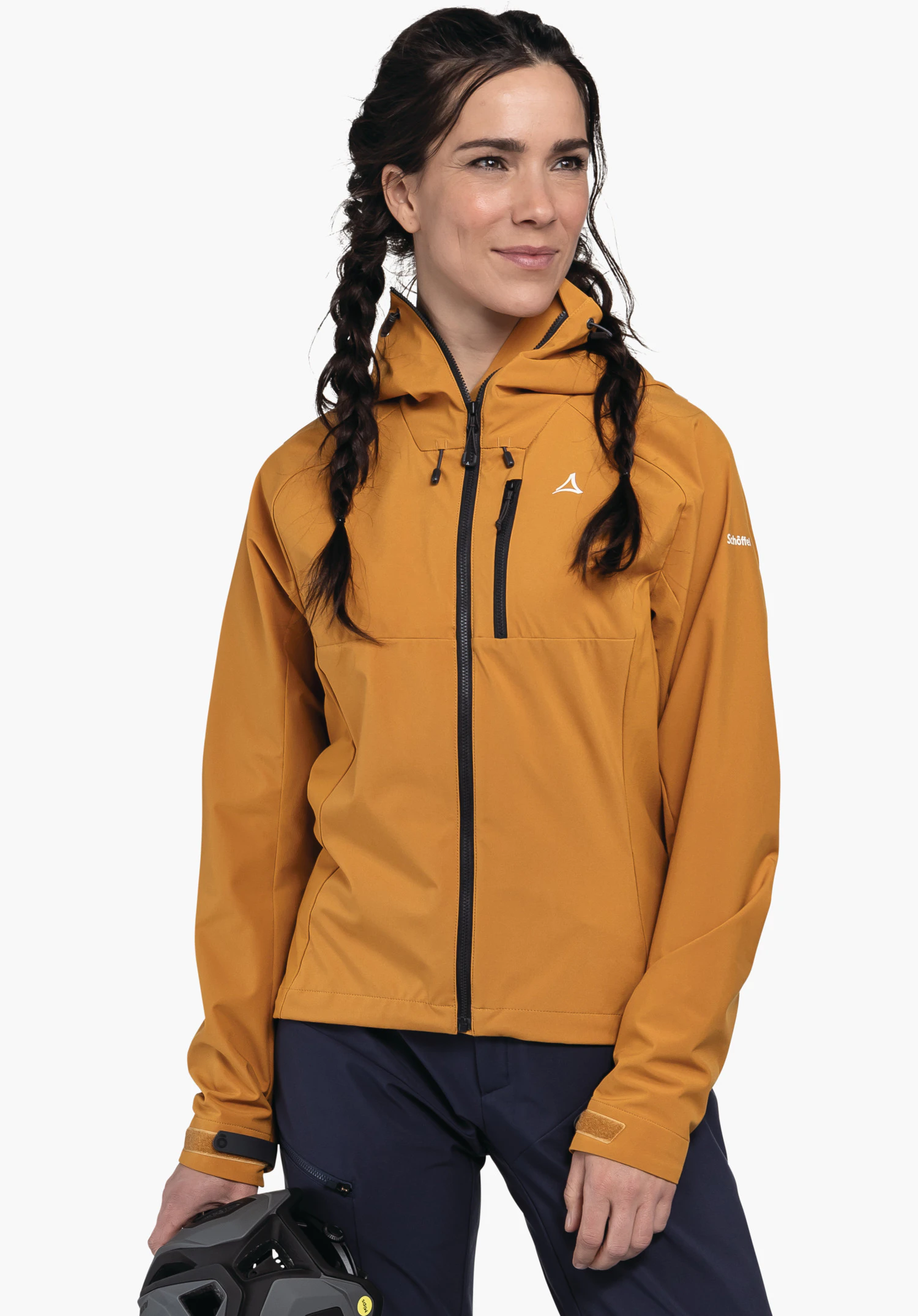 Hybrid Jk Style Salza WMS femme portant une veste jaune foncé avec logo Schöffel, tenant un casque gris dans la main gauche; debout devant un fond blanc. Texte sur la manche:"Schöffel".
