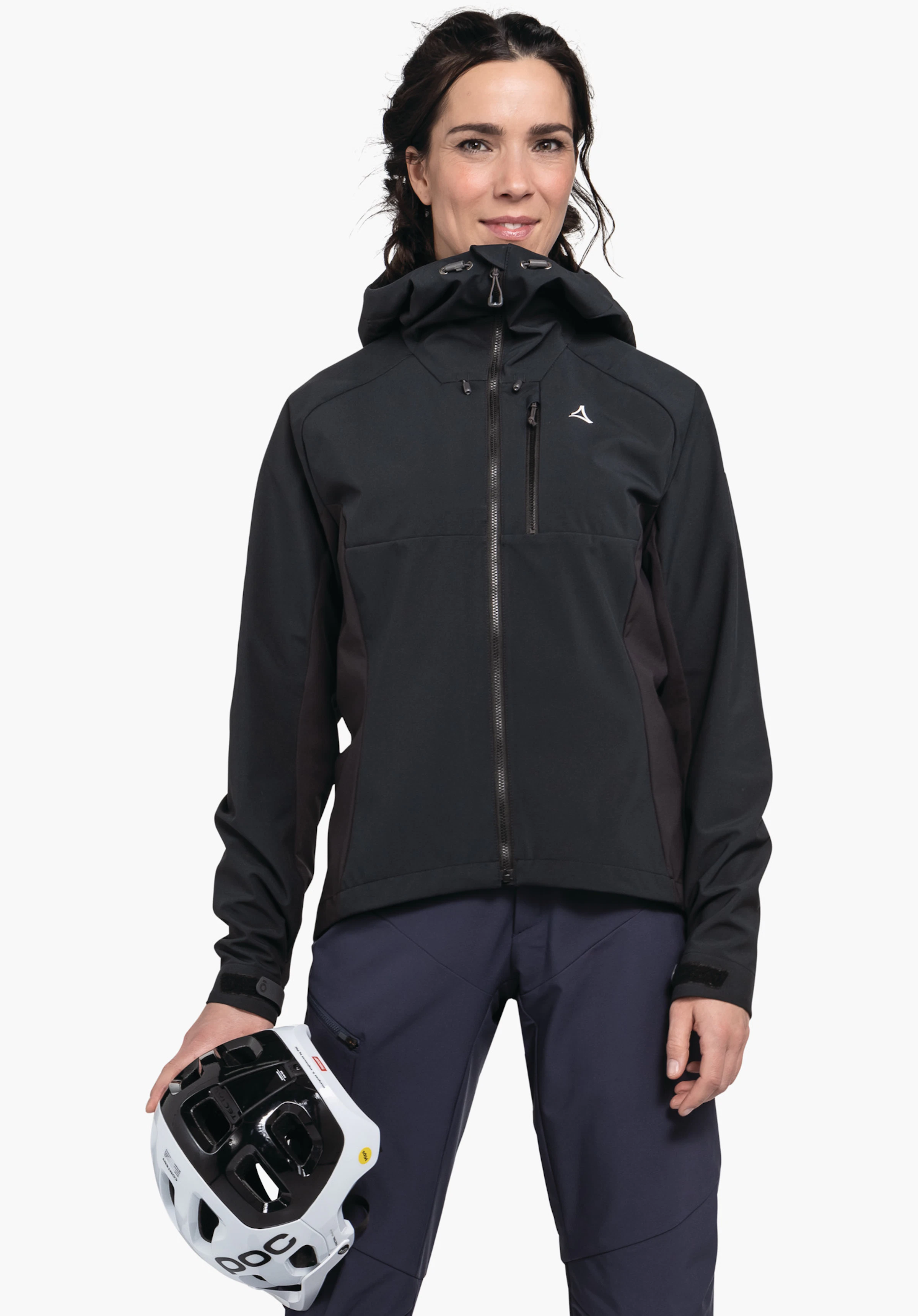 Hybrid Jk Style Salza WMS Frau trägt schwarze Jacke mit Schöffel-Logo, hält weißen Helm mit schwarzer Aufschrift "POC"; steht vor hellem Hintergrund.