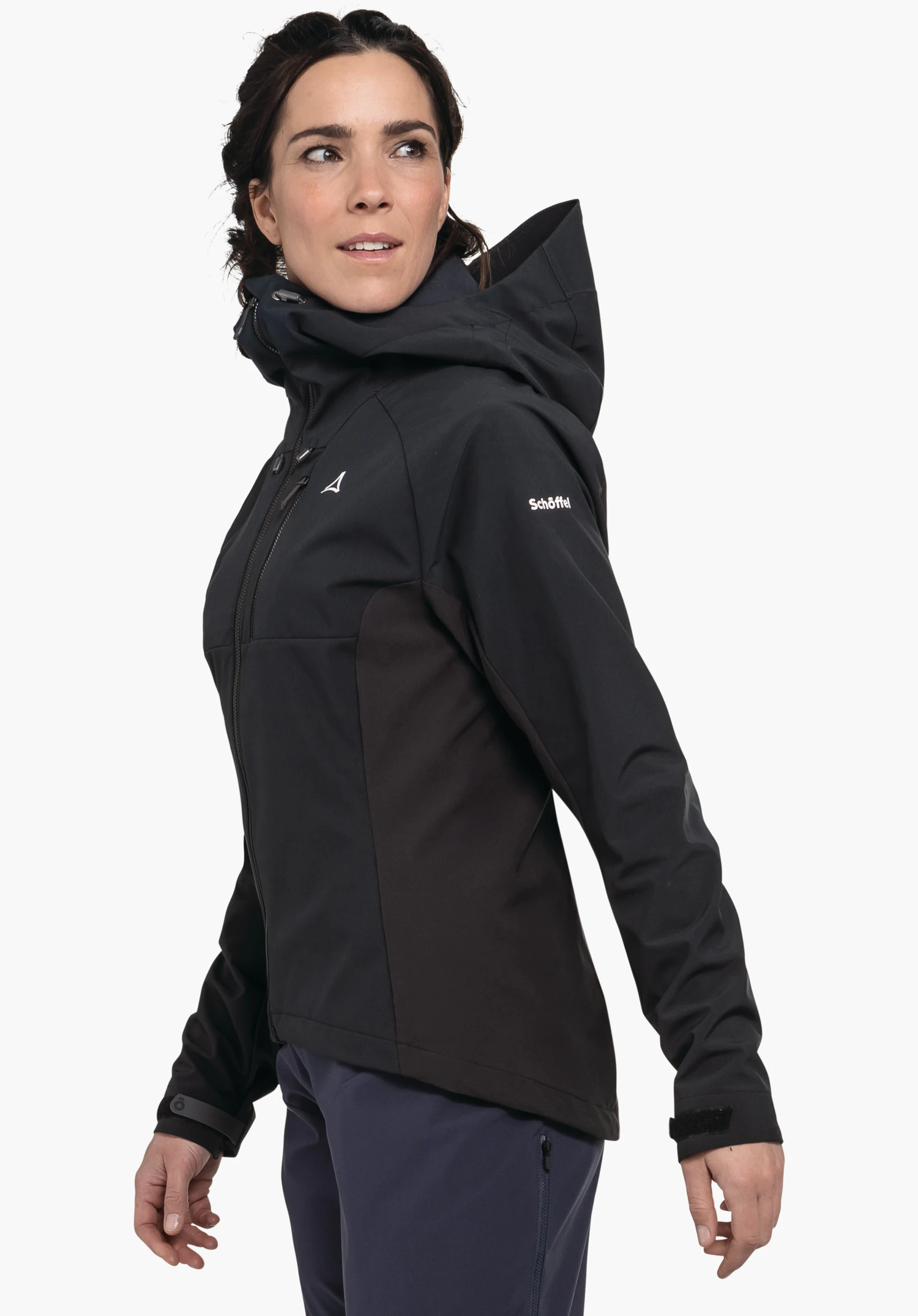 Hybrid Jk Style Salza WMS Frau in schwarzer Kapuzenjacke dreht den Kopf nach rechts und blickt seitlich; Schöffel-Logo auf der Brust, Schriftzug "Schöffel" auf dem Ärmel; dunkelblaue Hose, einfarbiger Hintergrund.