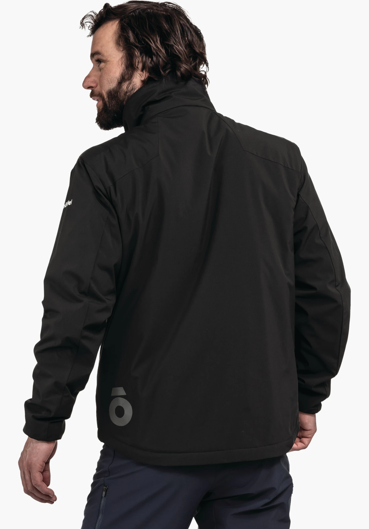 Ins Jacket Style Salza MNS veste noire portée par un homme se détournant légèrement; debout devant un fond blanc; inscription blanche "Schöffel" sur la manche gauche; pantalon bleu foncé.