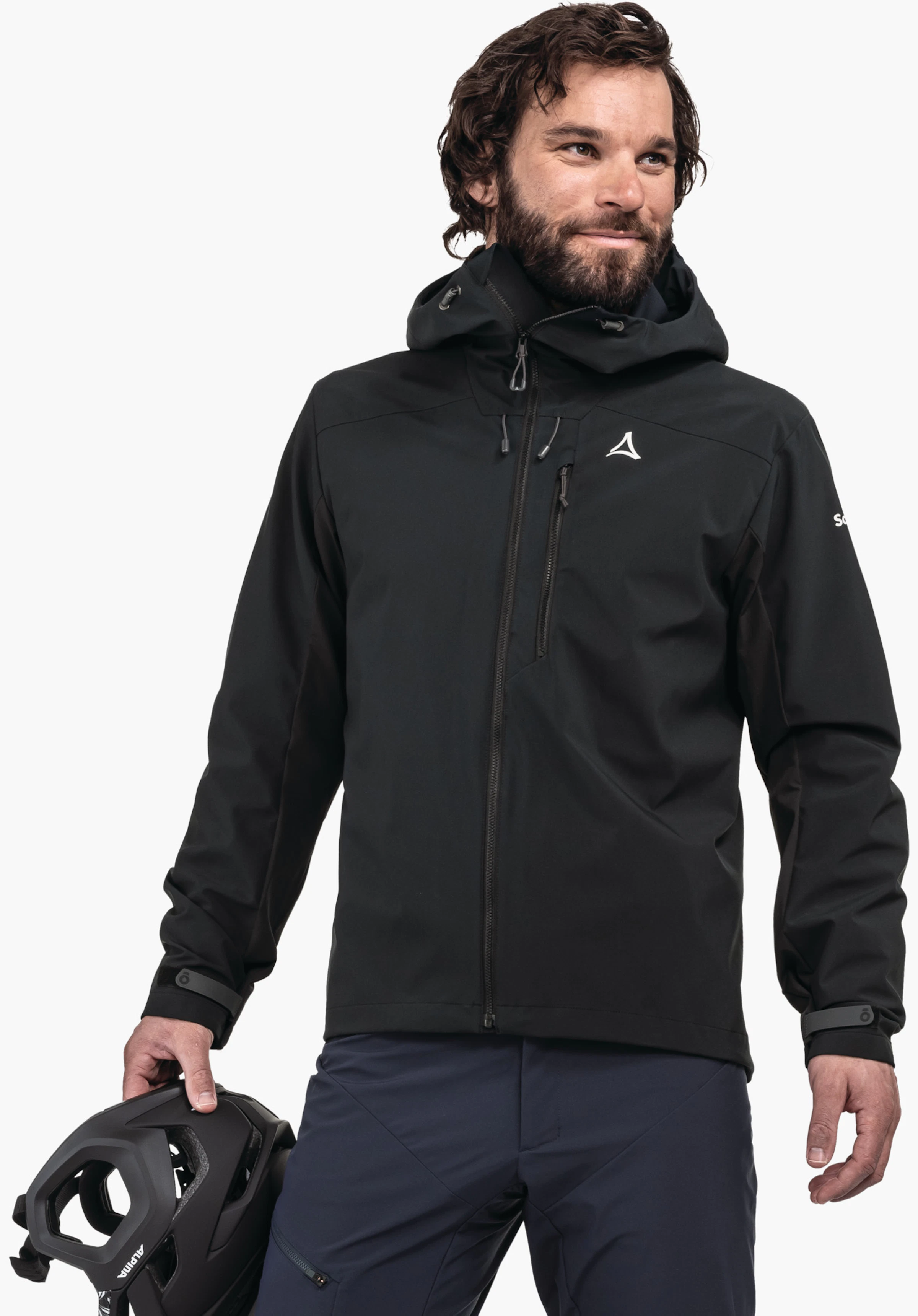Hybrid Jk Style Salza MNS veste noire à capuche avec logo Schöffel sur la poitrine, portée par un homme tenant un casque de vélo noir; debout devant un fond clair neutre. Texte sur la manche:"Schöffel"; inscription sur le casque:"ALPINA".