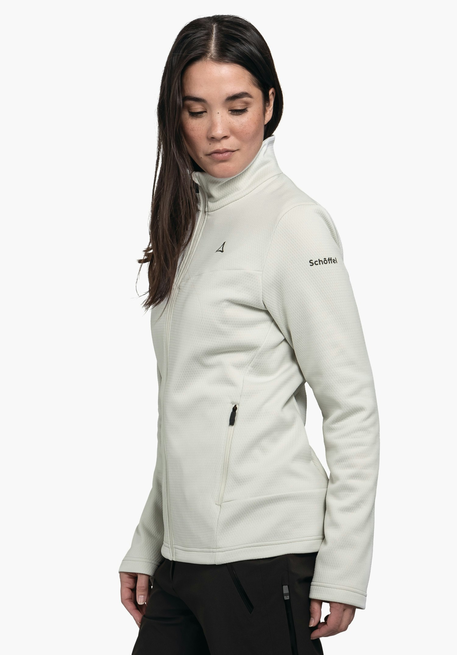 Fleece Jk Style Pine WMS veste polaire noire foncée, portée par une personne debout de profil regardant en haut à gauche; pantalon bleu clair, fond blanc. Texte sur la manche: "Schöffel".