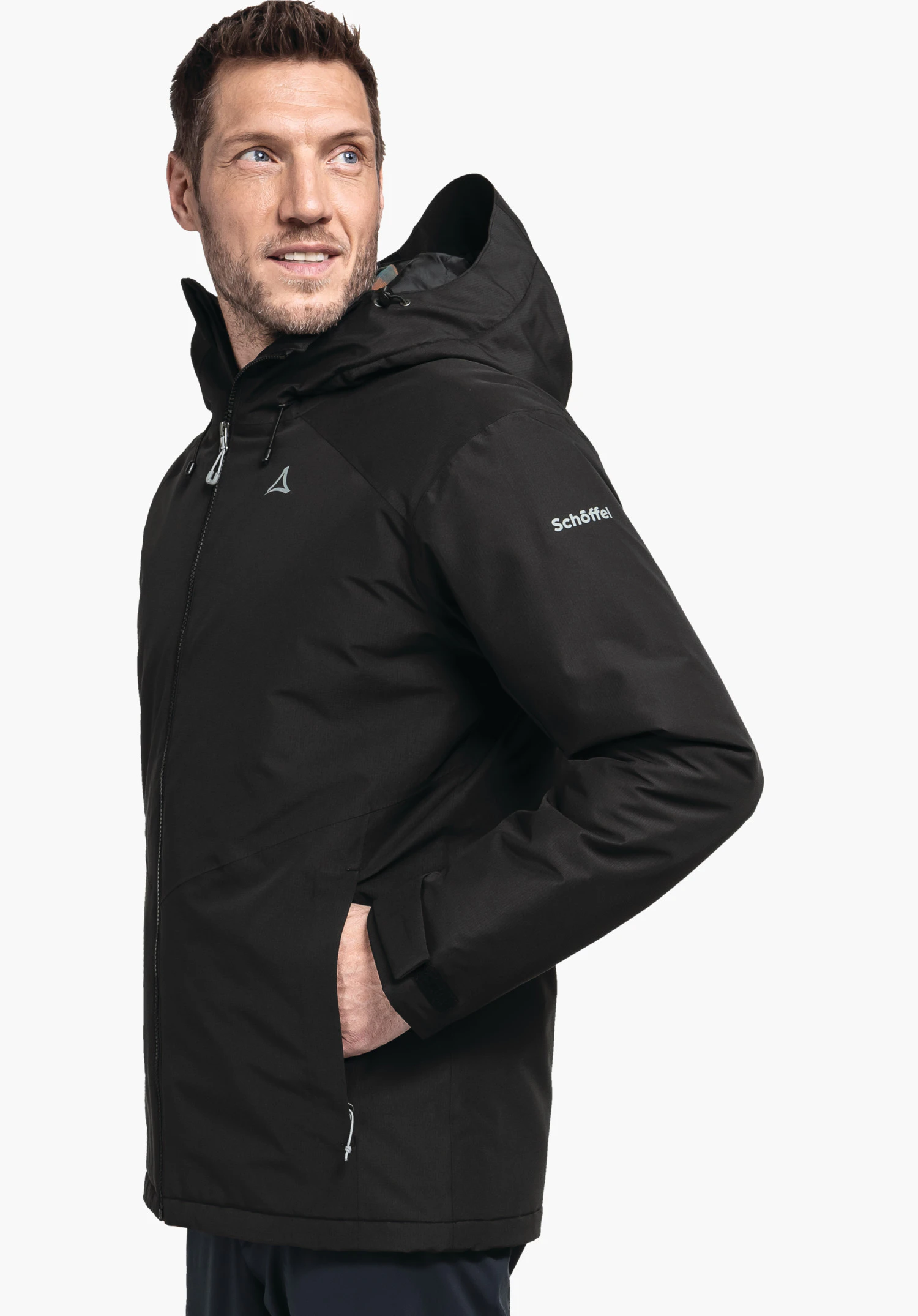 Ins Jacket Style Wildkar MNS Schwarze Kapuzenjacke mit Schöffel-Logo auf Brust und Schriftzug Schöffel auf dem Ärmel, von einem Mann getragen, Hand in Tasche, stehender Blick, weißer Hintergrund.