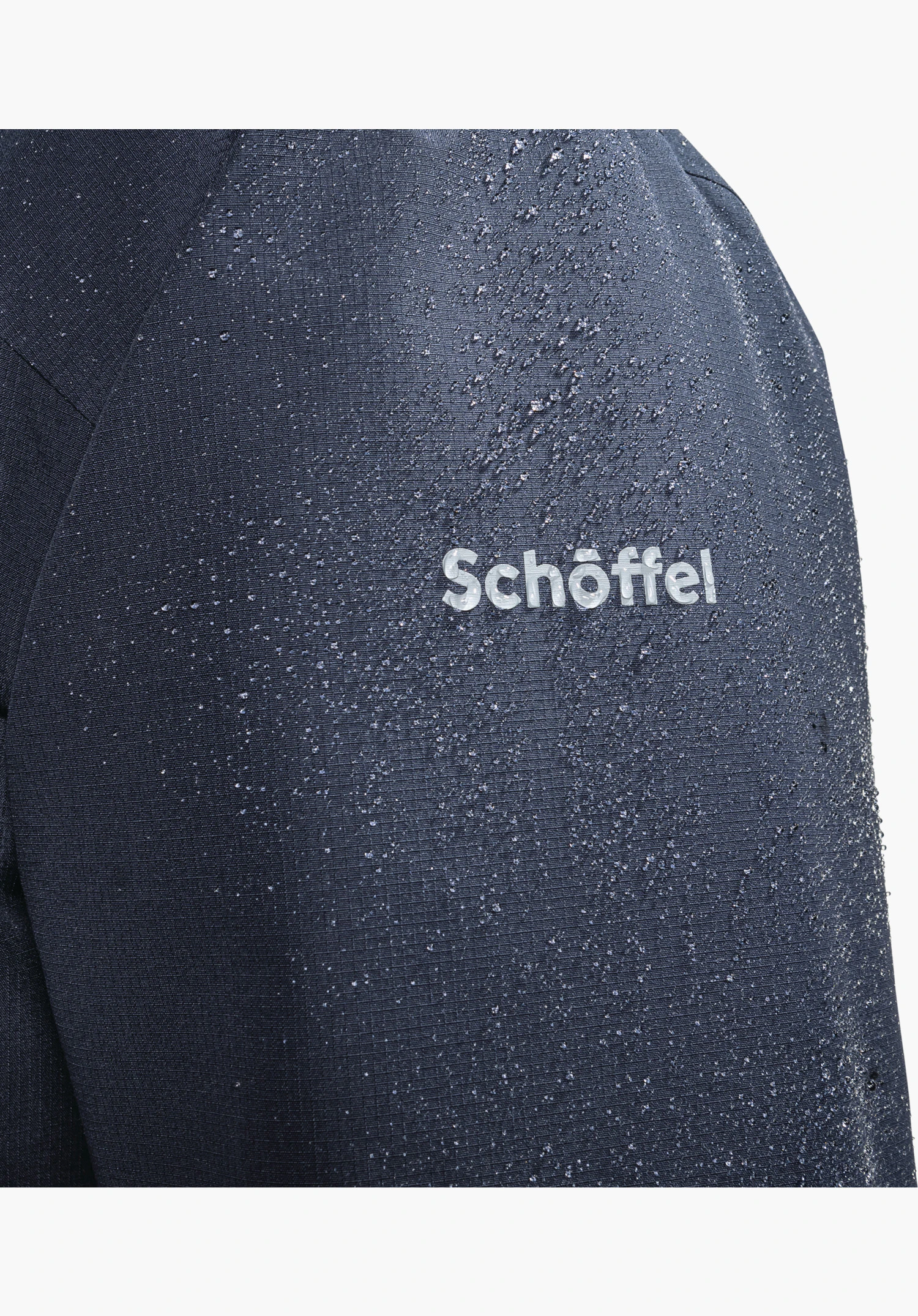 Ins Jacket Style Wildkar MNS zeigt das wasserabweisende blaue Material mit Wassertropfen und dem Schöffel-Logo, Nahaufnahme vor weißem/neutralem Hintergrund.