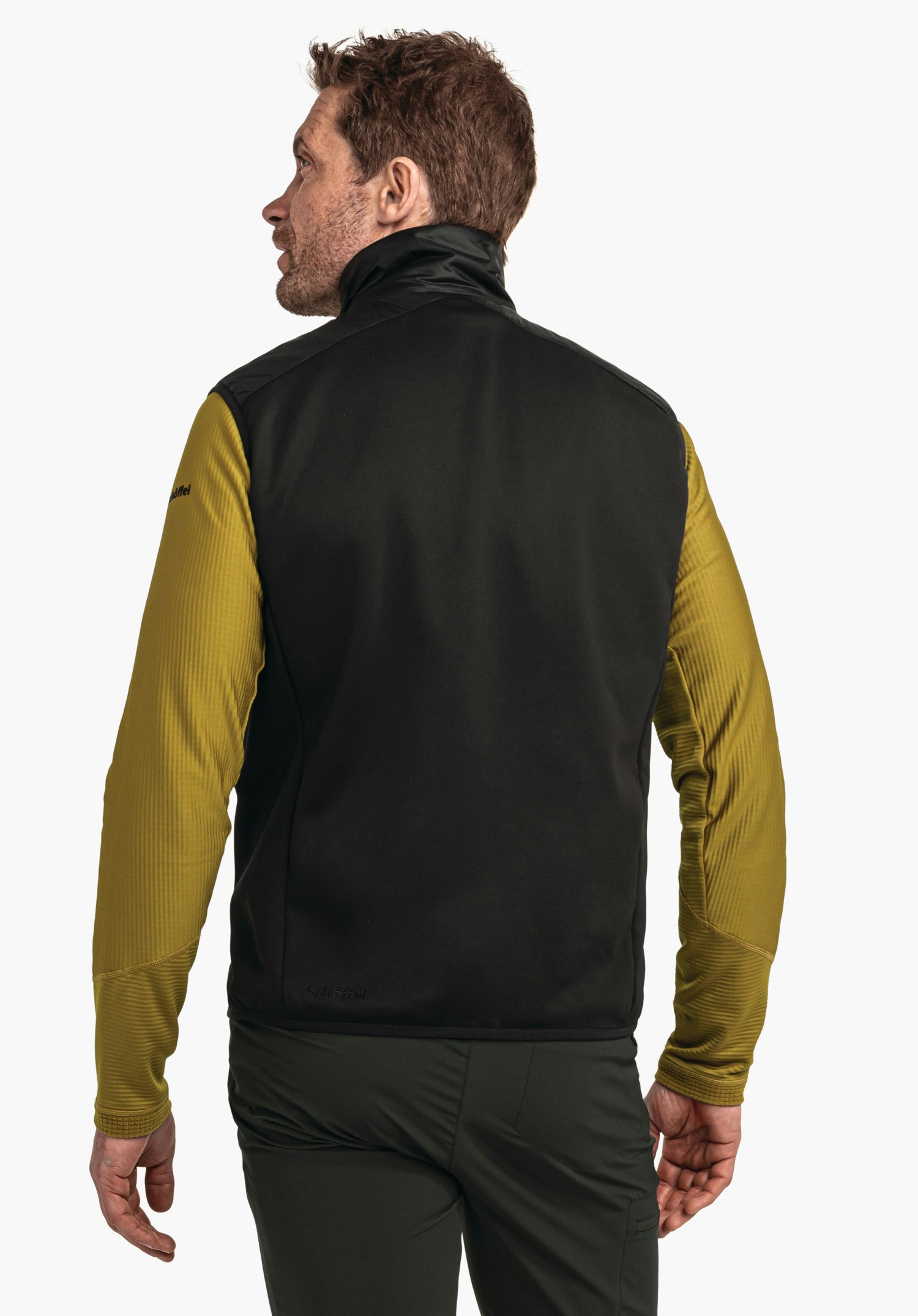 Hybrid Vt Style Cascata MNS gilet noir porté sur un haut à manches longues jaune foncé; un homme se tient debout et regarde par-dessus l’épaule gauche, devant un fond blanc. Texte sur le gilet: « Schöffel ».