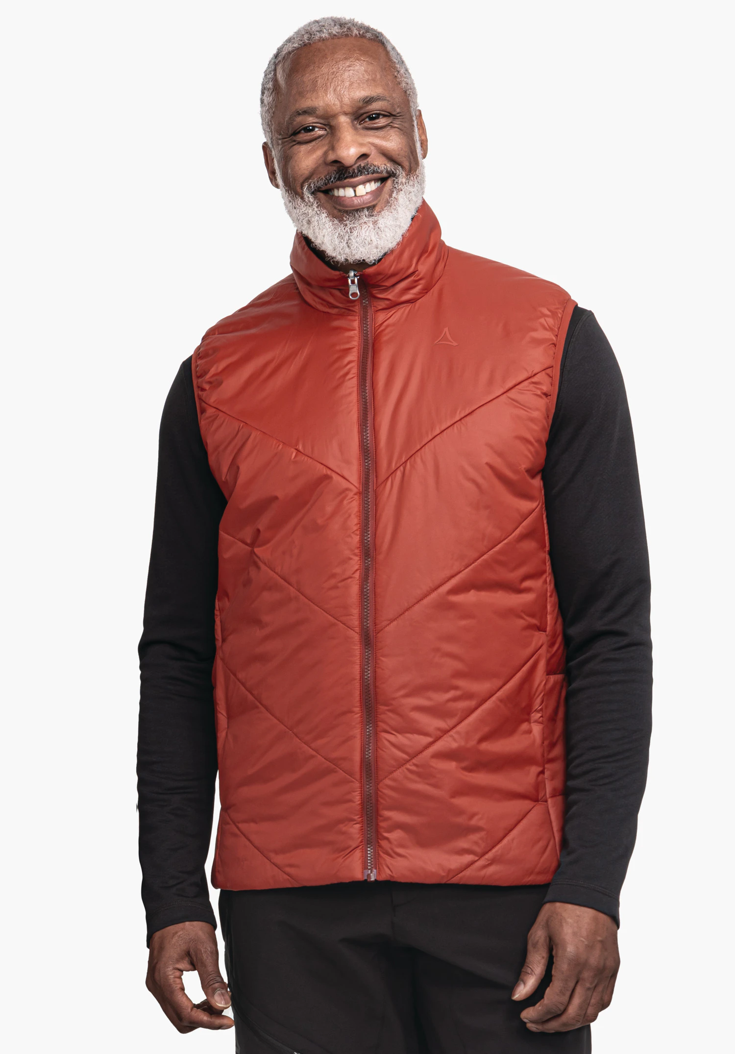 Ins Vest Style Yew MNS Rote Steppweste mit sichtbarem Schöffel-Logo, von lächelndem Mann getragen; steht frontal vor weißem Hintergrund, trägt darunter ein schwarzes Langarmshirt und schwarze Hosen.