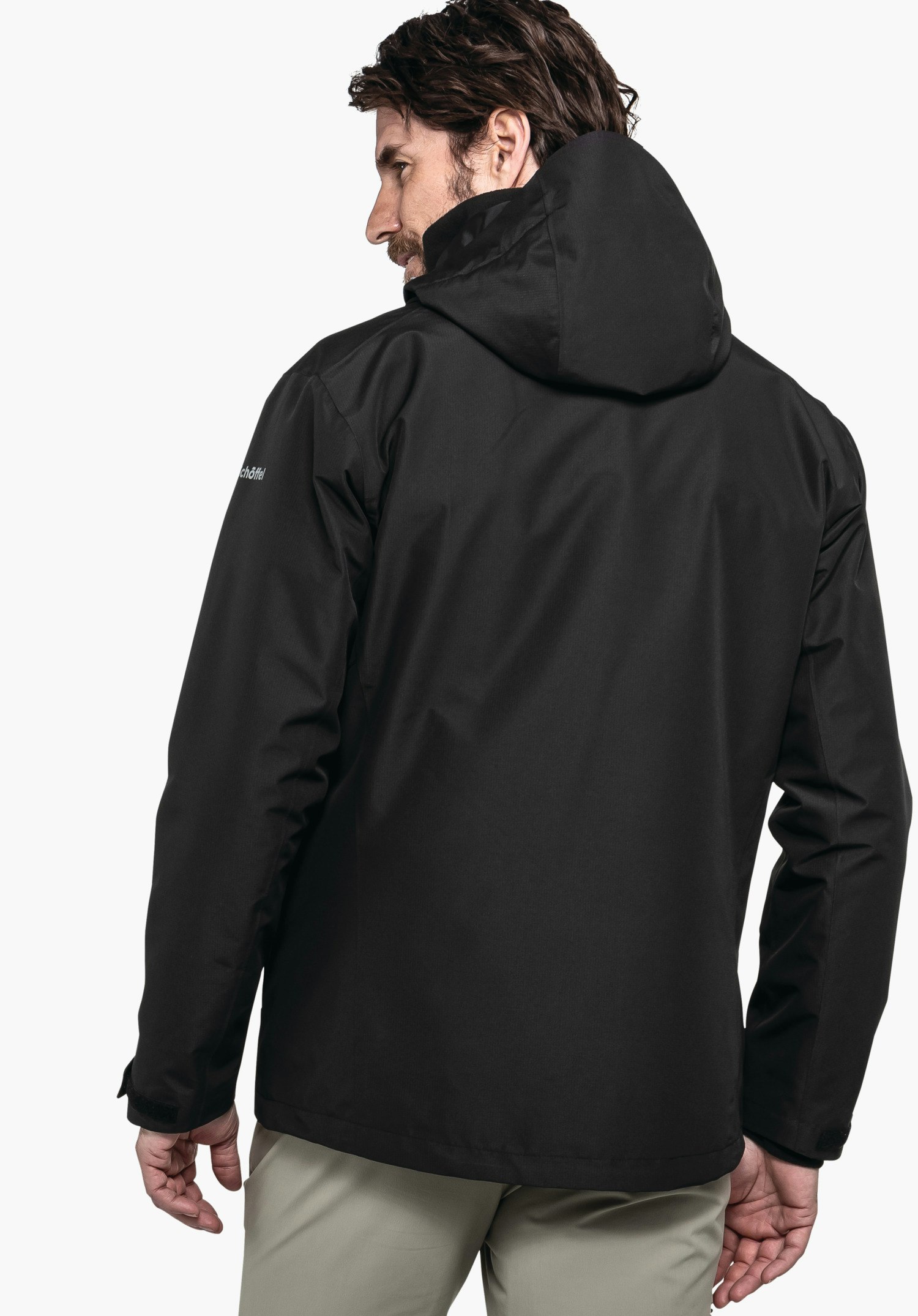 3in1 Jacket Style Okere MNS Schwarze Herrenjacke mit Kapuze, von hinten getragen; Person steht leicht seitlich vor weißem Hintergrund. Auf dem Ärmel steht: "schöffel".