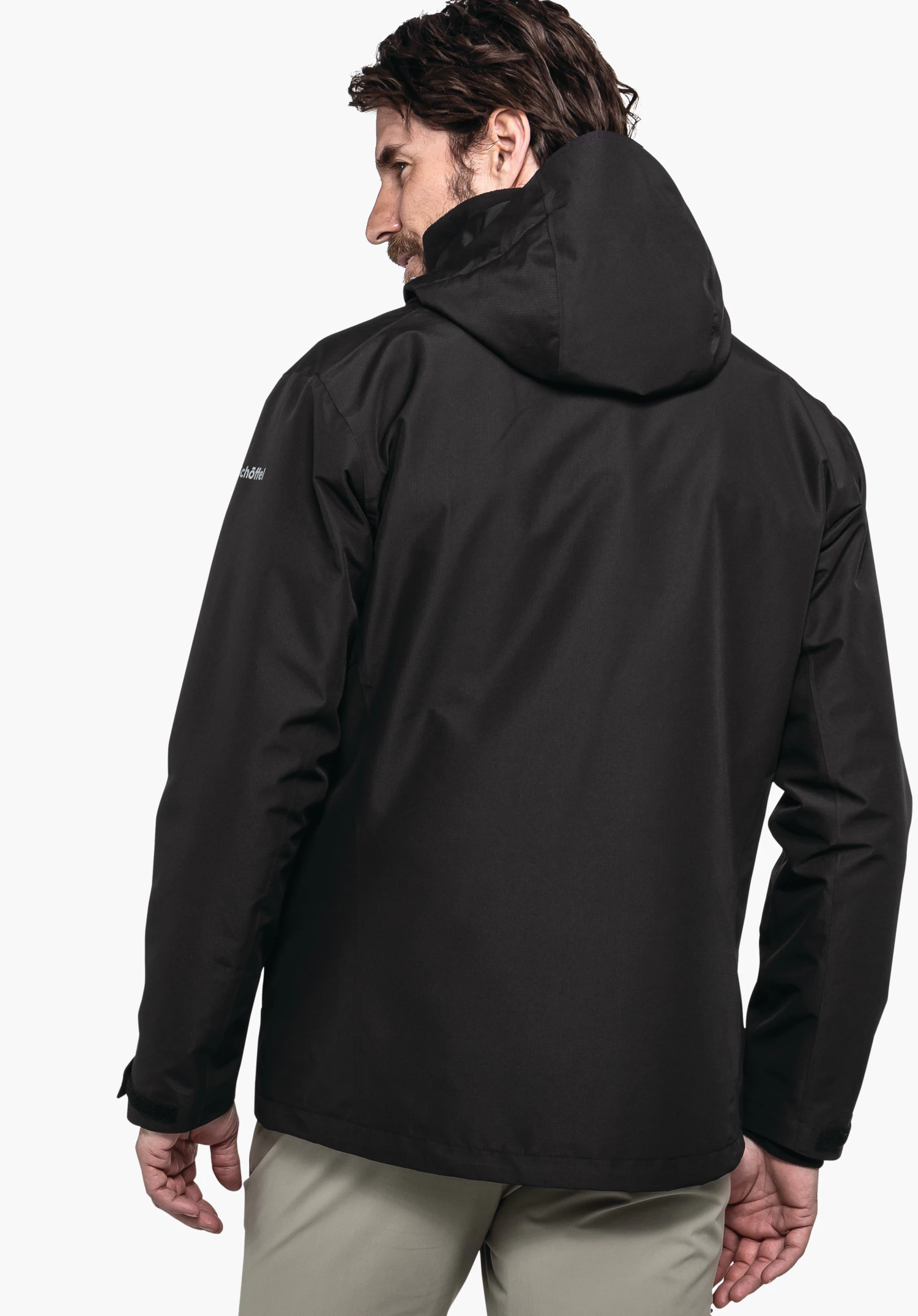 3in1 Jacket Style Okere MNS black men’s hooded jacket worn from the back; person stands slightly turned against a white background. Sleeve text: “schöffel”.