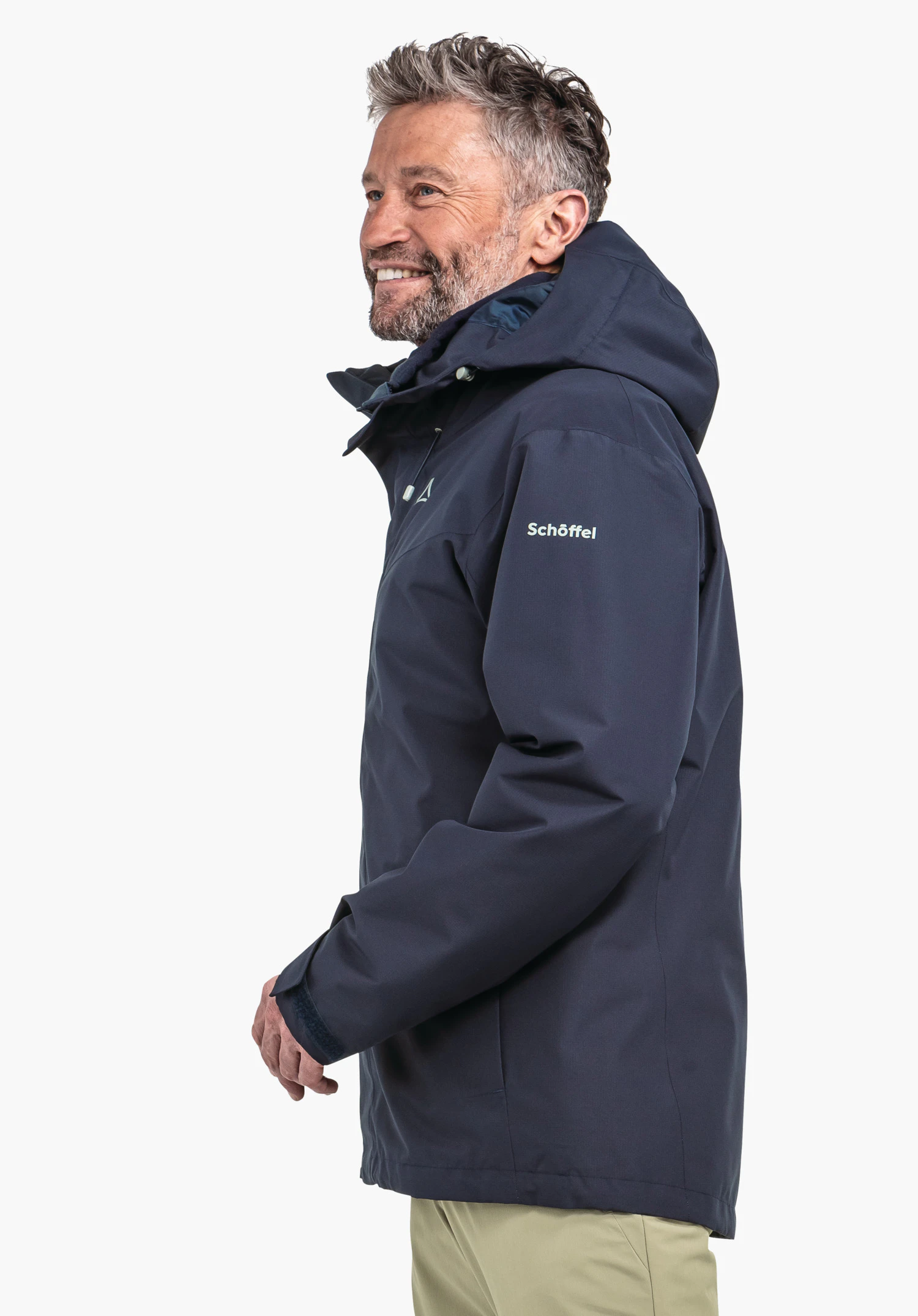 3in1 Jacket Style Okere MNS dark blue jacket worn by a man smiling in profile, hood raised, standing side-on in front of a white background; Schöffel logo visible on chest, lettering "Schöffel" on sleeve.