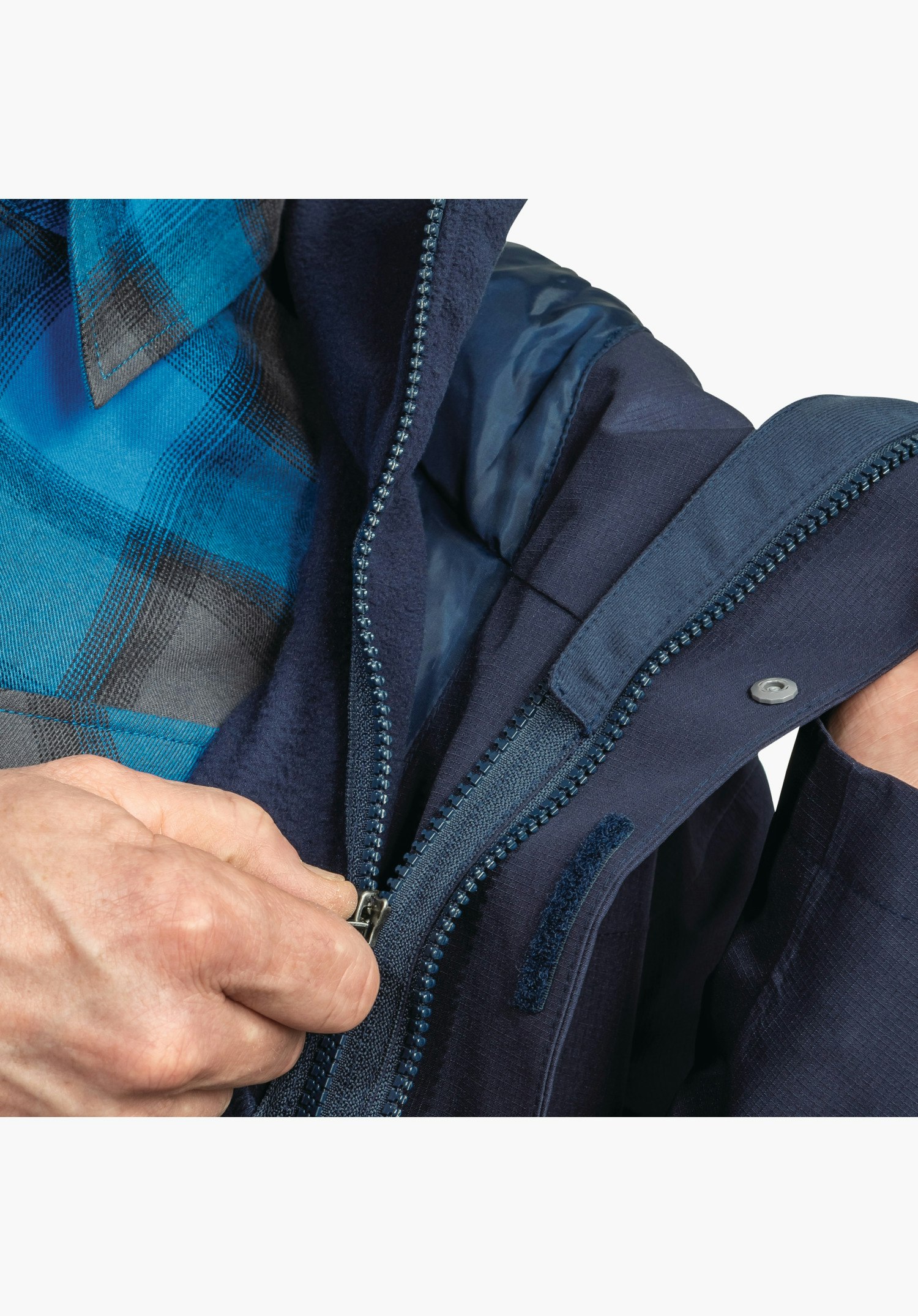 3in1 Jacket Style Okere MNS Detailansicht des blauen Reißverschluss-Systems, das Innen- und Außenjacke verbindet, ergänzt durch einen Druckknopf an der Leiste. Nahaufnahme vor weißem Hintergrund.