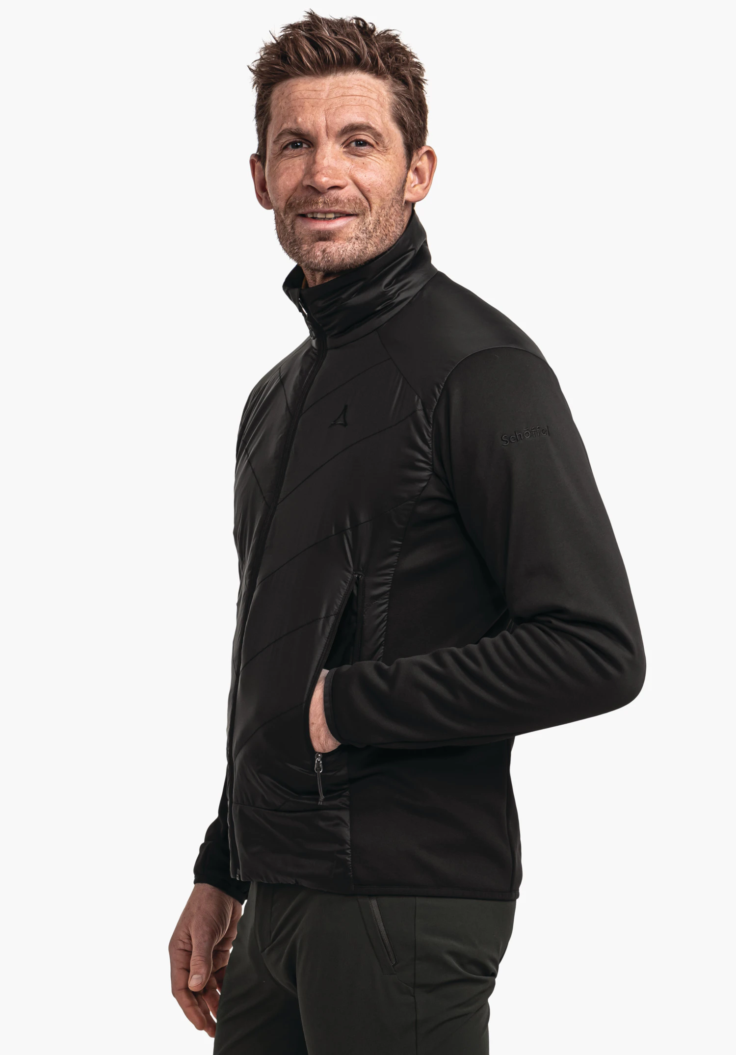 Hybrid Jk Style Cascata MNS zwarte jas, gedragen door een man die licht zijwaarts staat met één hand in de zak; Schöffel-logo op de borst, tekst "Schöffel" op de mouw; witte achtergrond.