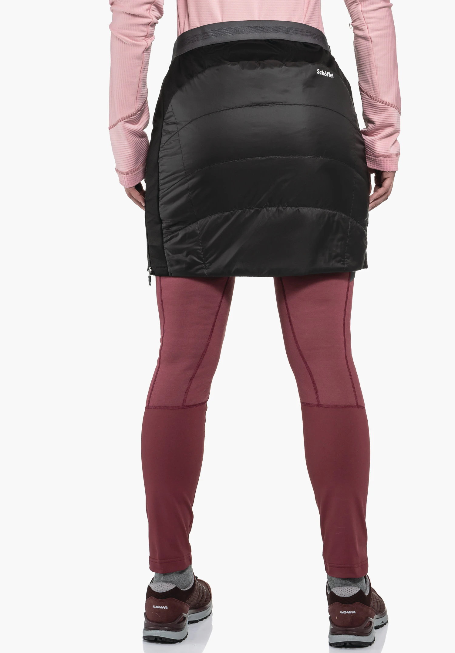 Ins Skirt Style Cascata WMS zwarte gewatteerde heuprok, gedragen over donkerrode leggings; persoon staat achterwaarts voor een witte achtergrond. Tekst: "Schöffel" op de rok, "LOWA" op de schoenen.