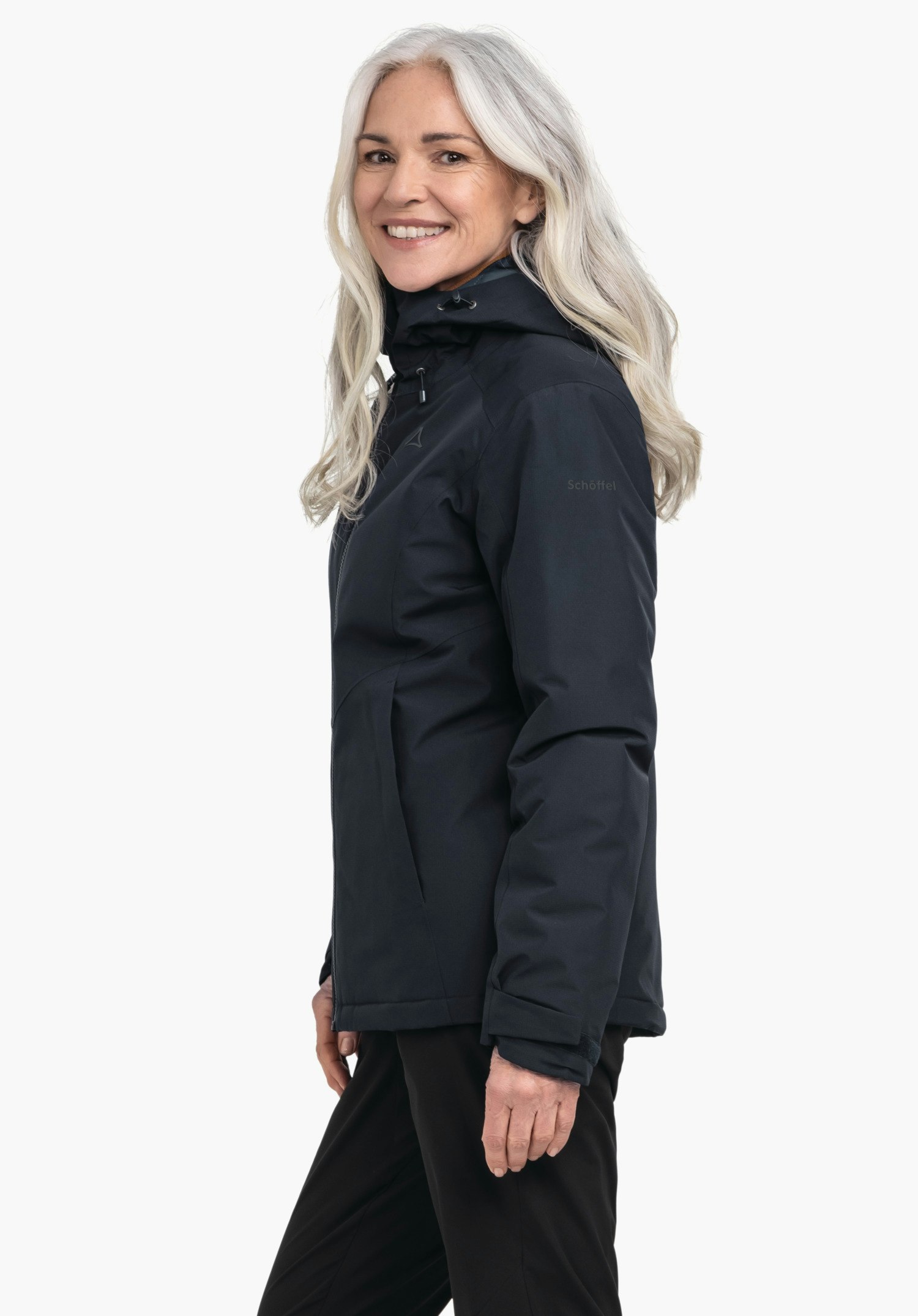 Ins Jacket Style Wildkar WMS Frau trägt dunkelblau Jacke mit Kapuze, lächelt und steht seitlich vor hellem Hintergrund; Schöffel-Logo auf Brust, Schriftzug "Schöffel" auf Ärmel.