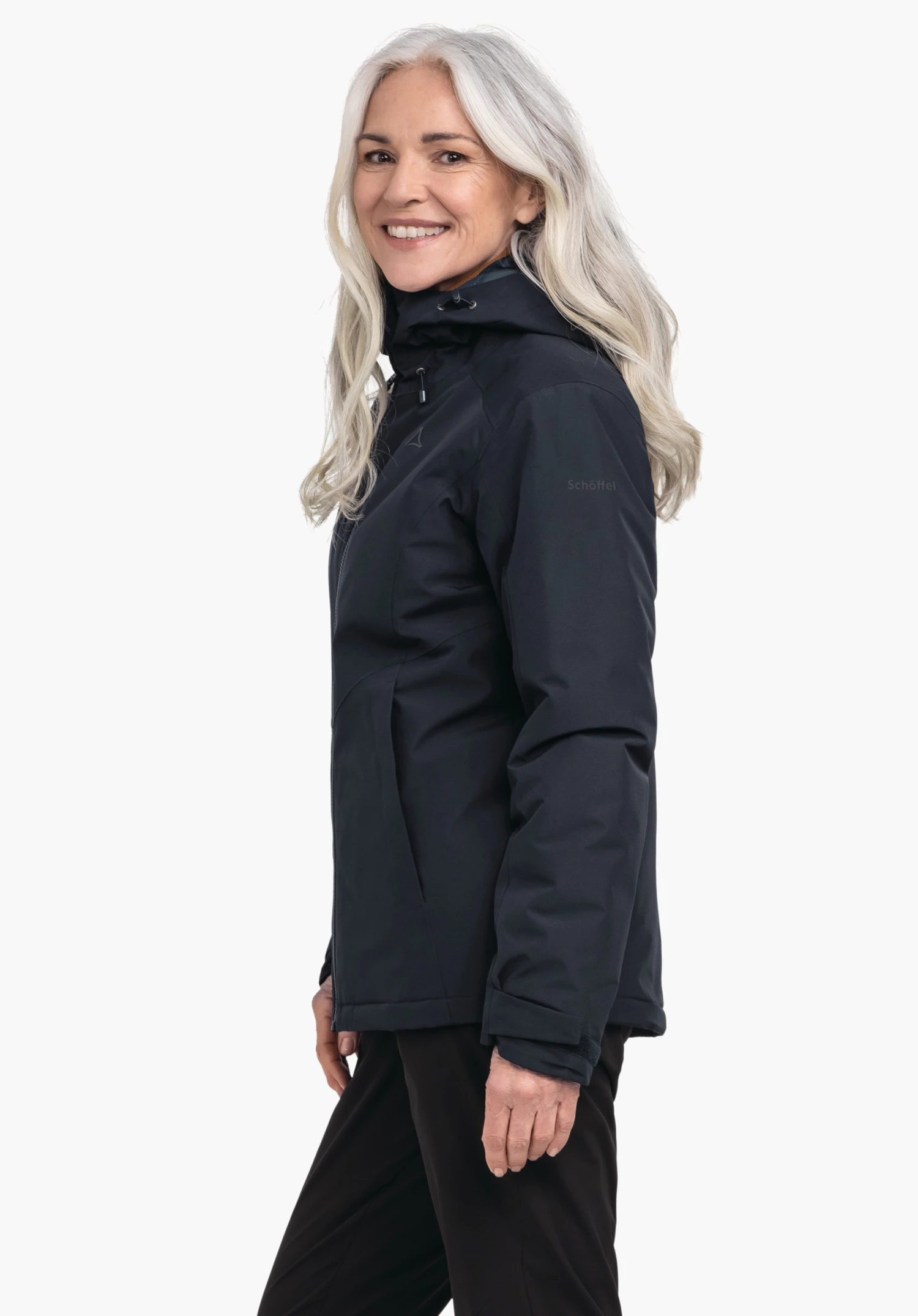 Ins Jacket Style Wildkar WMS vrouw draagt een donkerblauwe jas met capuchon, glimlacht en staat zijwaarts voor een lichte achtergrond; Schöffel-logo op de borst, tekst "Schöffel" op de mouw.
