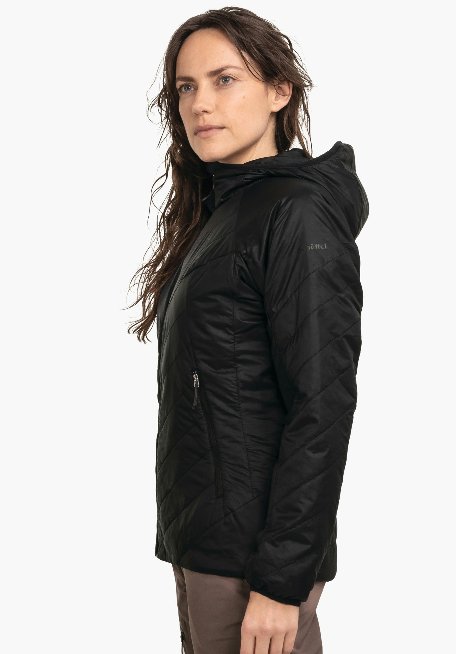 Ins Jacket Style Cascata WMS veste noire à capuche portée par une femme en position latérale, debout calmement devant fond clair; matière matelassée, poche zippée latérale. Texte sur la manche: "schöffel".