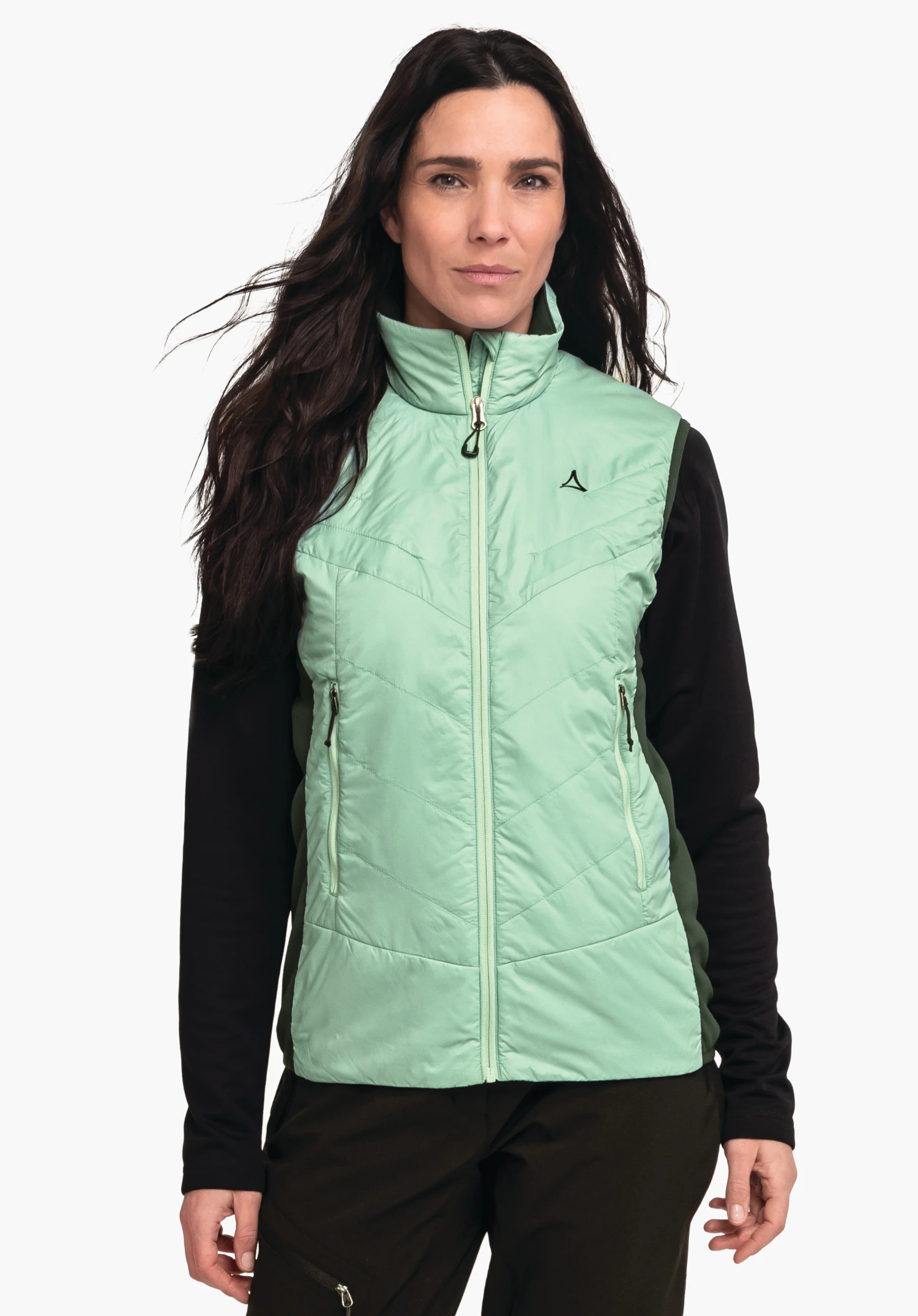 Hybrid Vt Style Cascata WMS Gilet vert clair zippé avec logo Schöffel sur la poitrine; porté par une femme, complété par des manches noires et un pantalon vert foncé devant un fond clair.