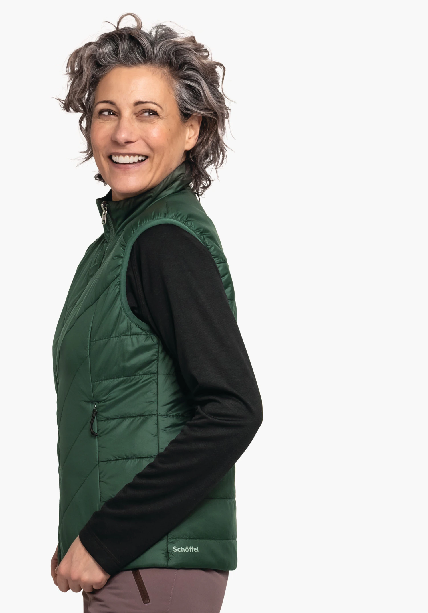 Ins Vest Style Yew WMS woman smiles side-on wearing a dark green quilted vest over a black long-sleeve shirt, standing in front of a light background. Text: Schöffel.